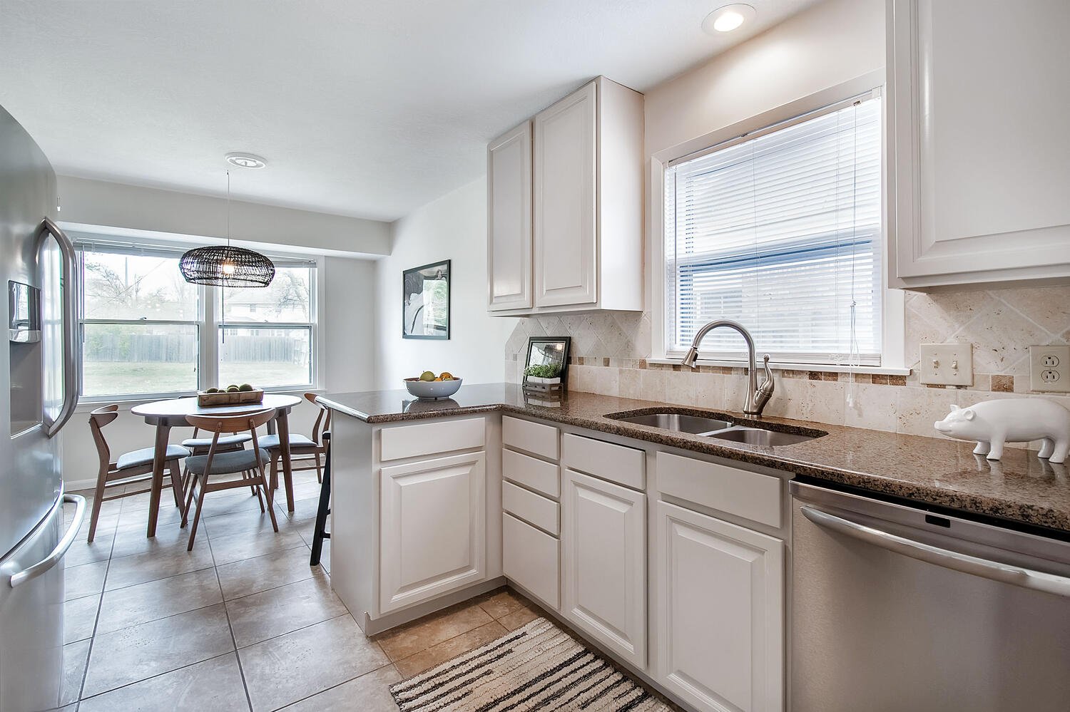 Modern kitchen with white cabinets, granite countertops, stainless steel appliances, a window above the sink, and a dining area with a round table and four chairs.