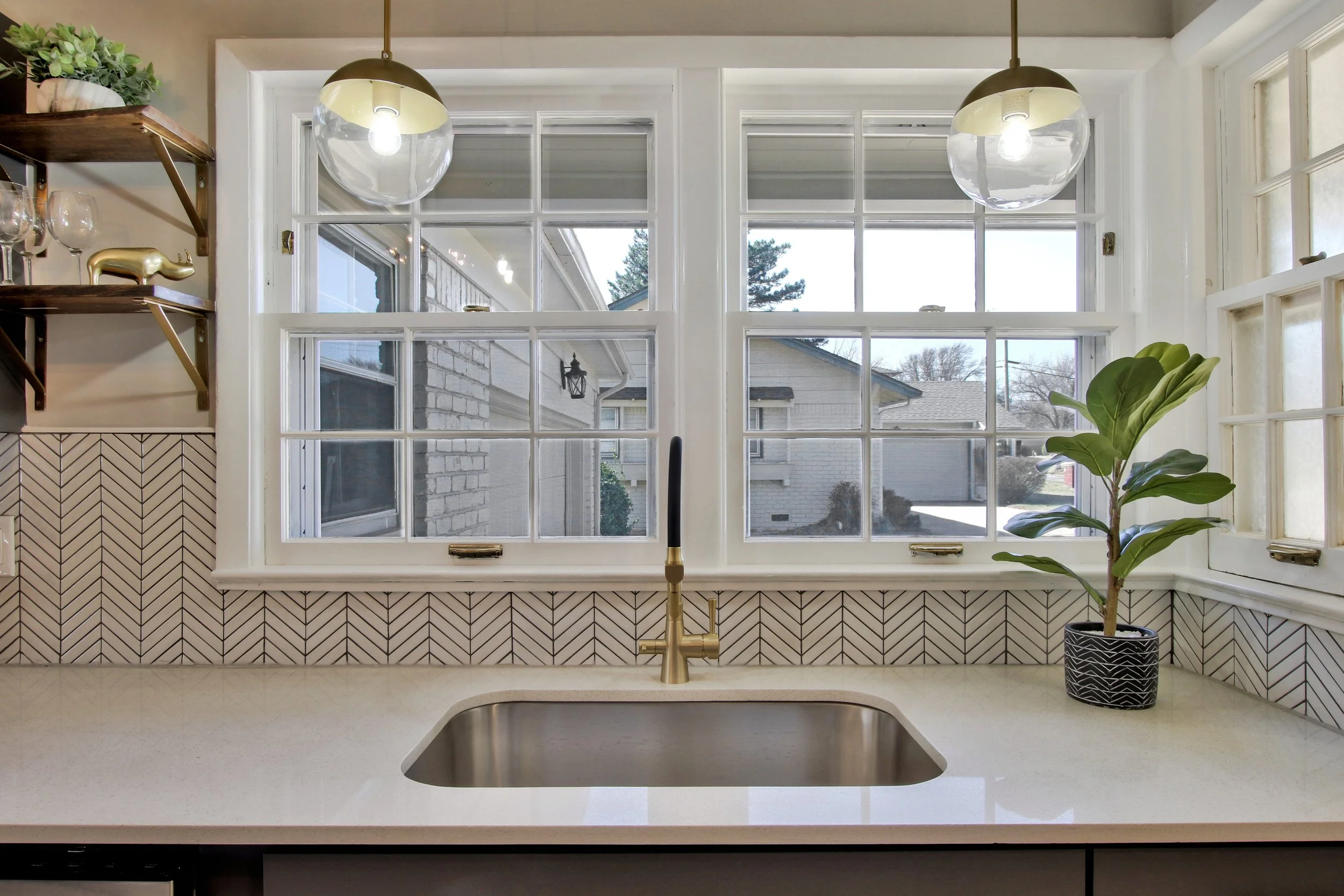 Indoor kitchen sink area with a window above, a potted plant on the right, and glass pendant lights hanging from the ceiling.