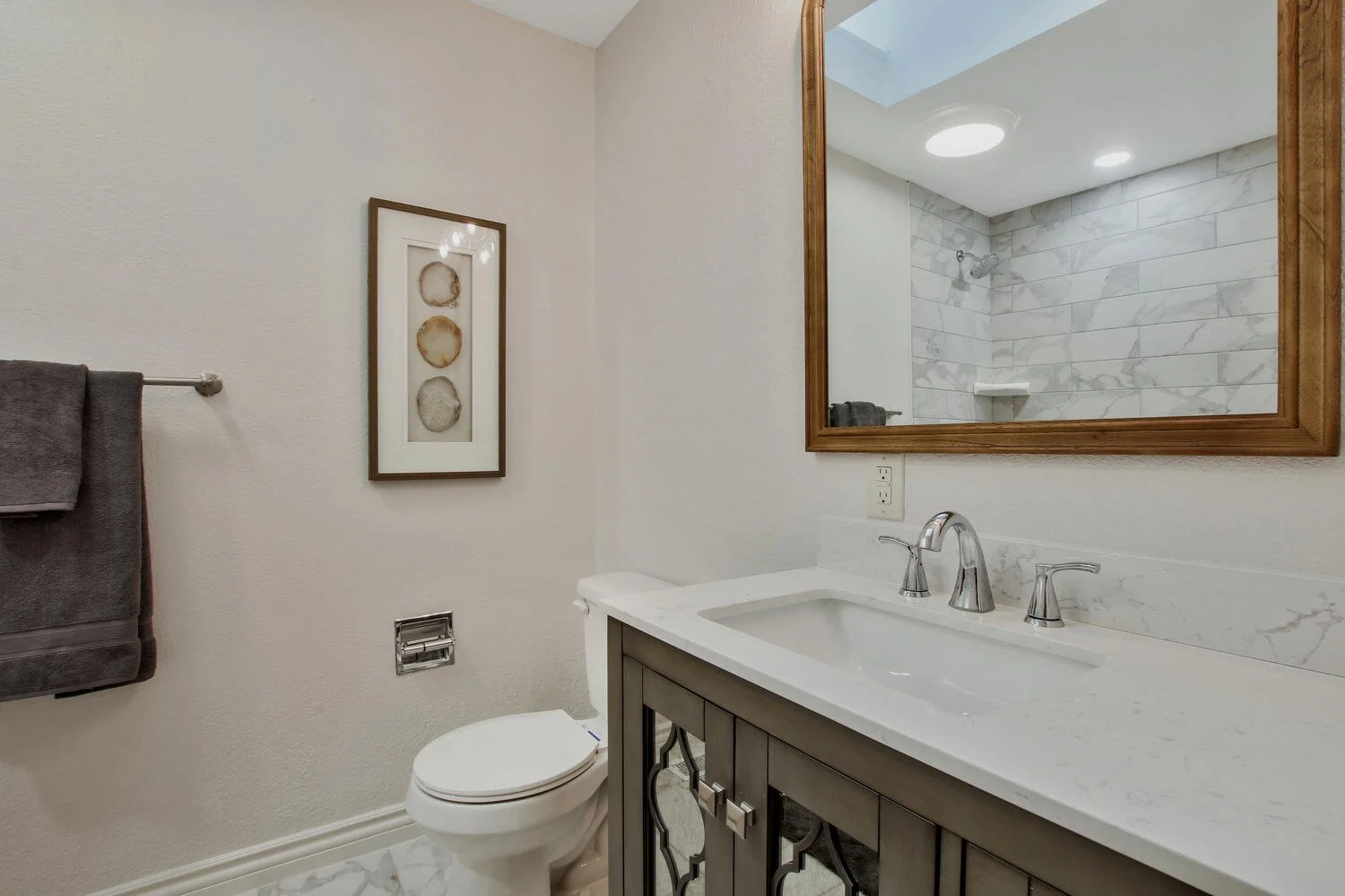 Bathroom with white walls, a toilet, a dark wood vanity with a white marble countertop, a large mirror, and a shower with marble tile walls.