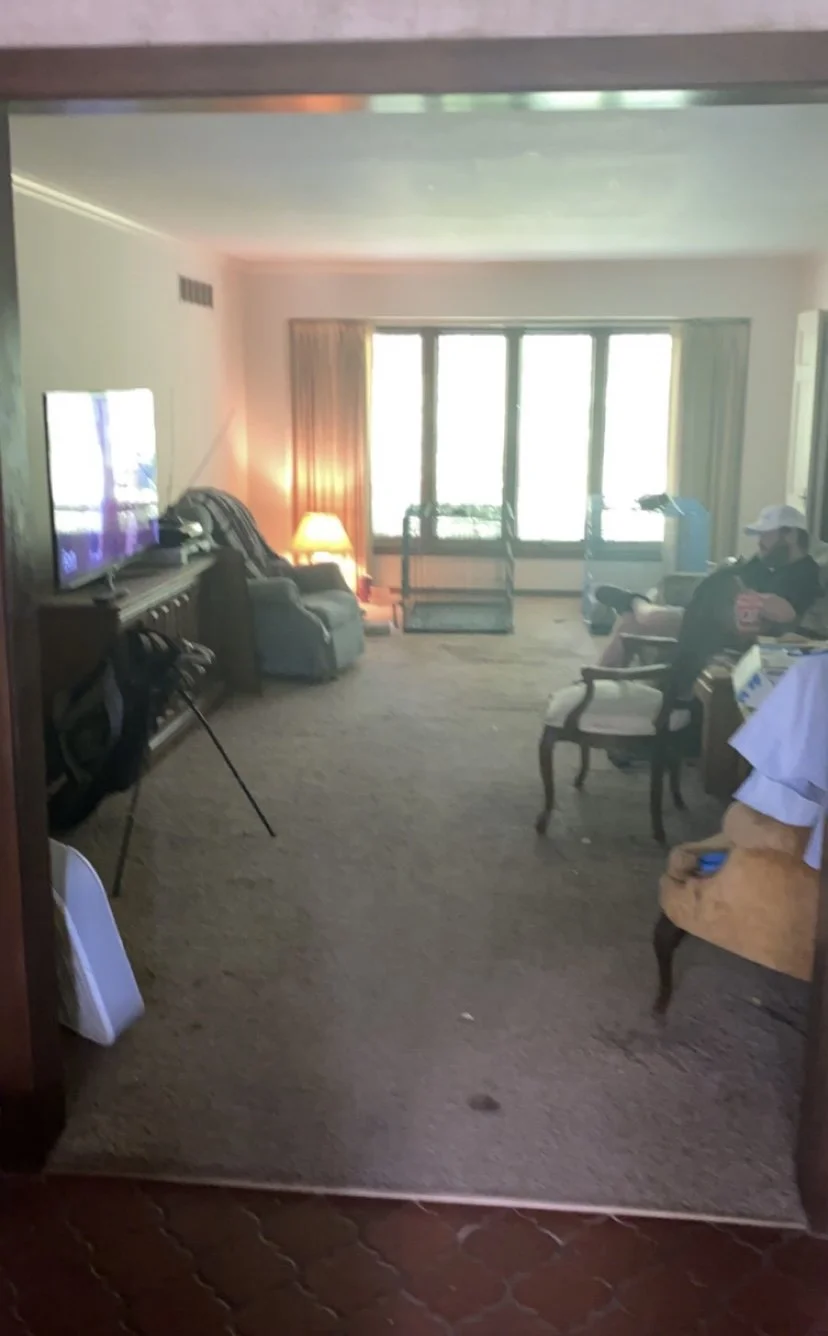 Hotel room with armchair, television, window with curtains, and man sitting on armchair.