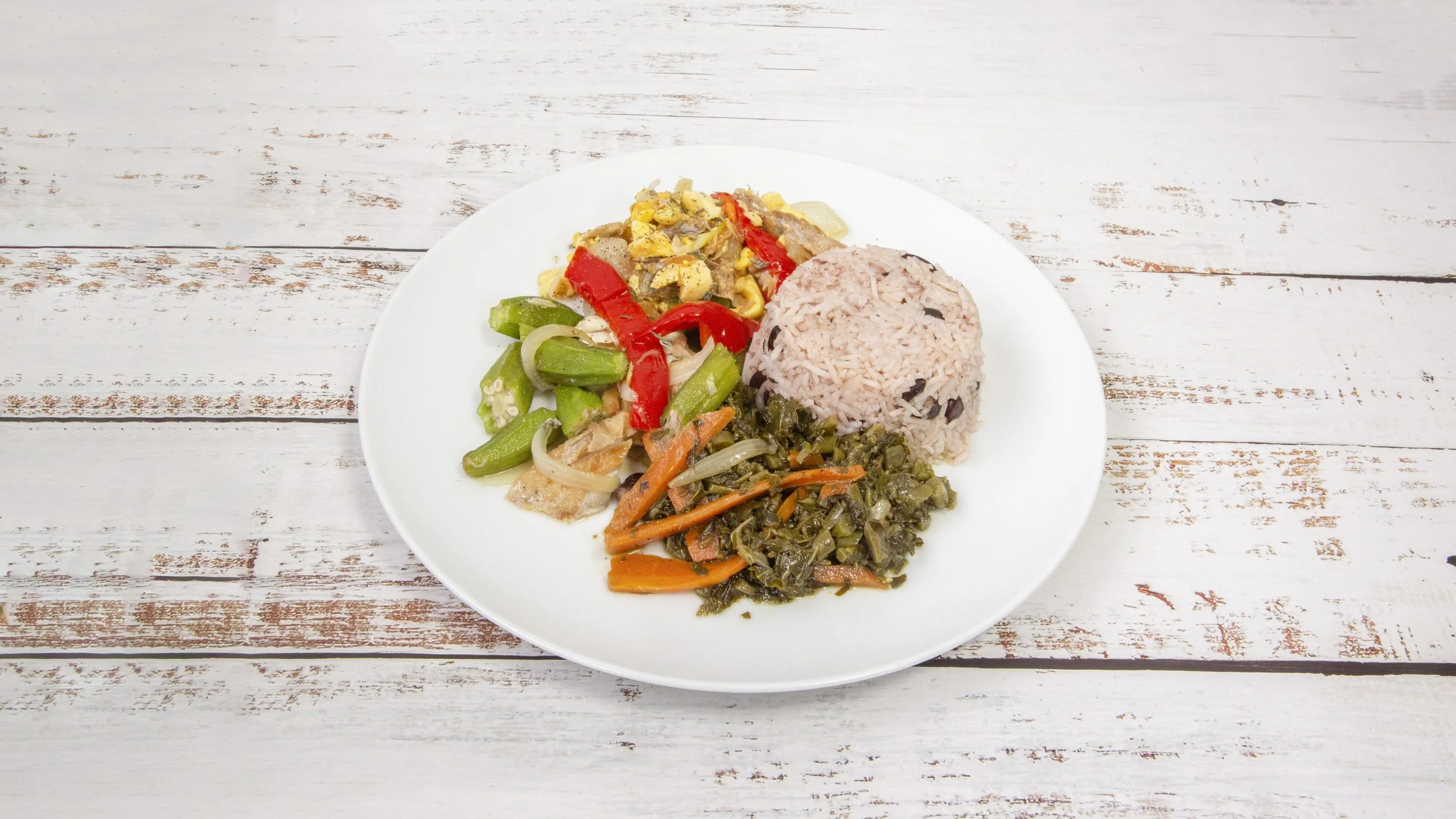 A plate of Jamaican rice and peas with cooked greens, stir-fried vegetables, and saltfish.