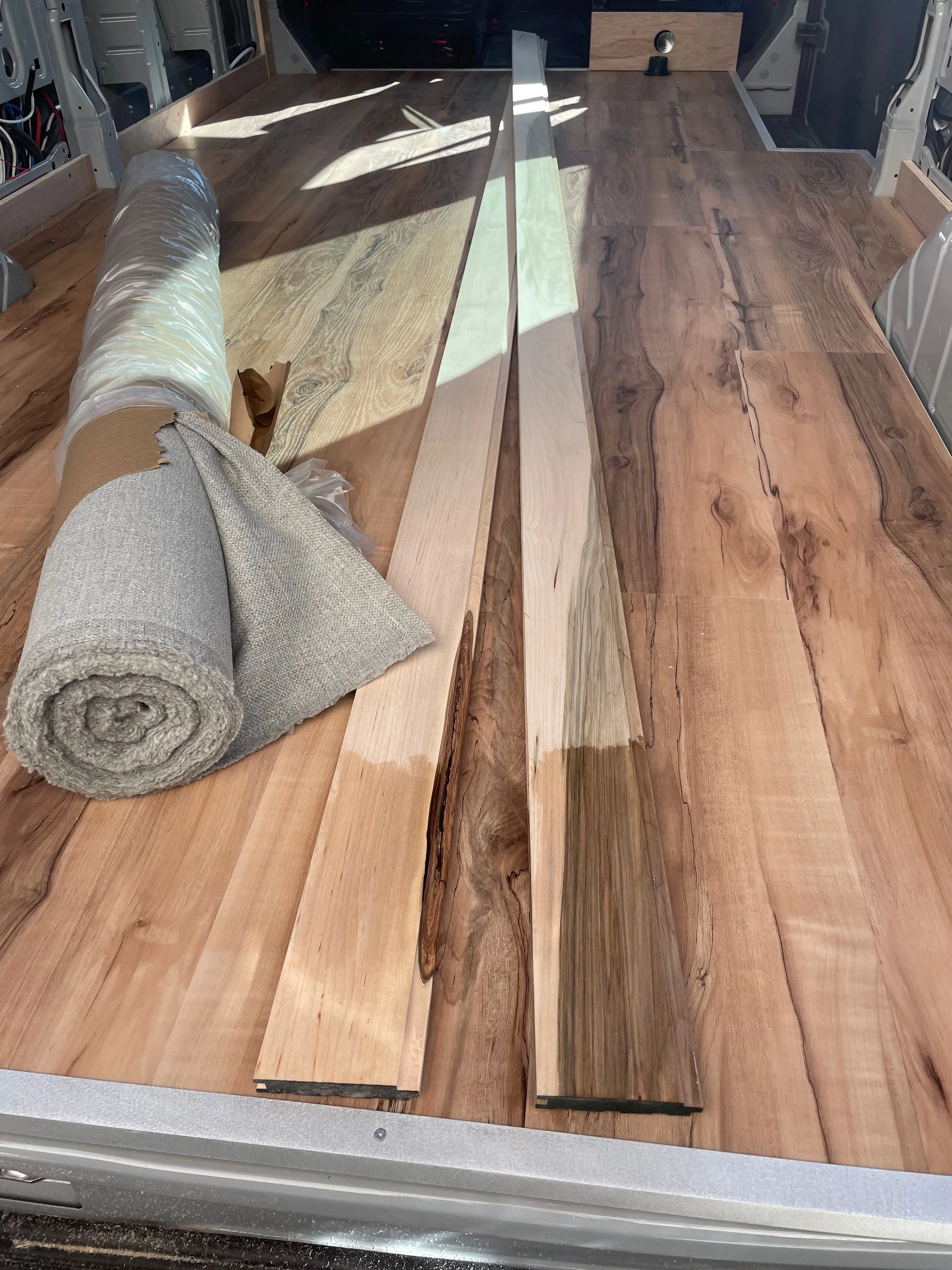Wooden flooring materials, including a roll of carpet and planks of wood, being prepared for installation inside a vehicle.