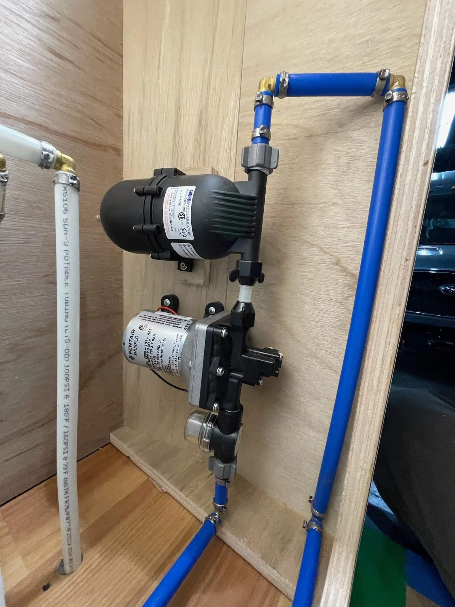 Water pump system with blue and white pipes, mounted on a wooden panel