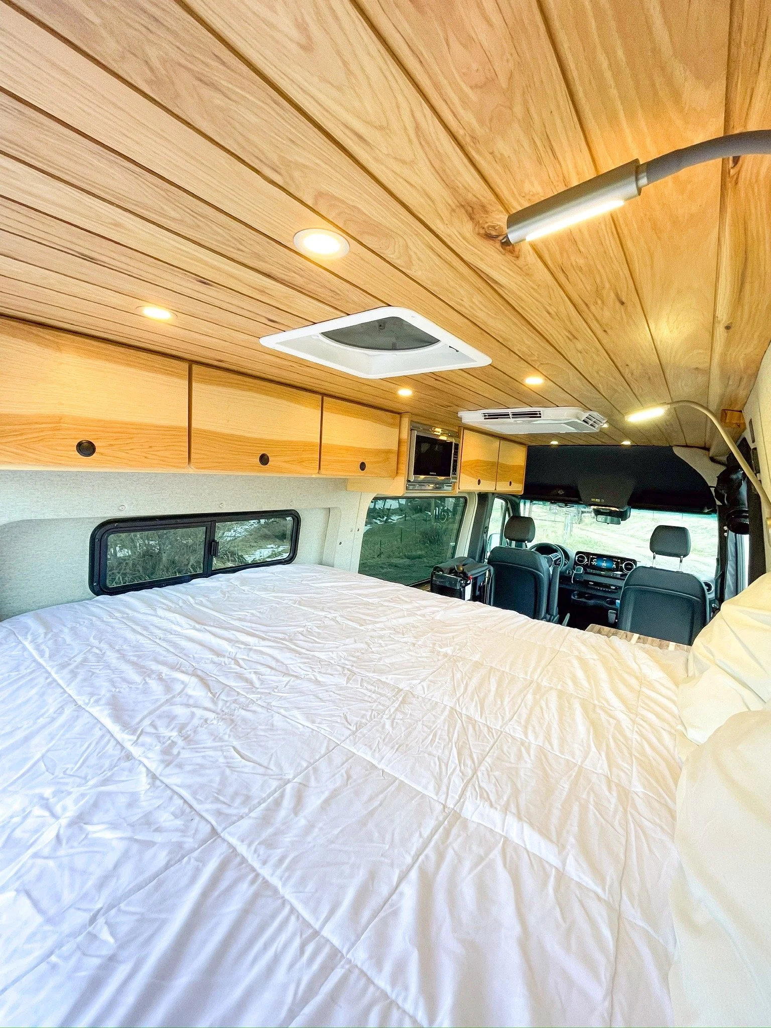 Interior of camper van with wooden ceiling, bedding, and storage cabinets.