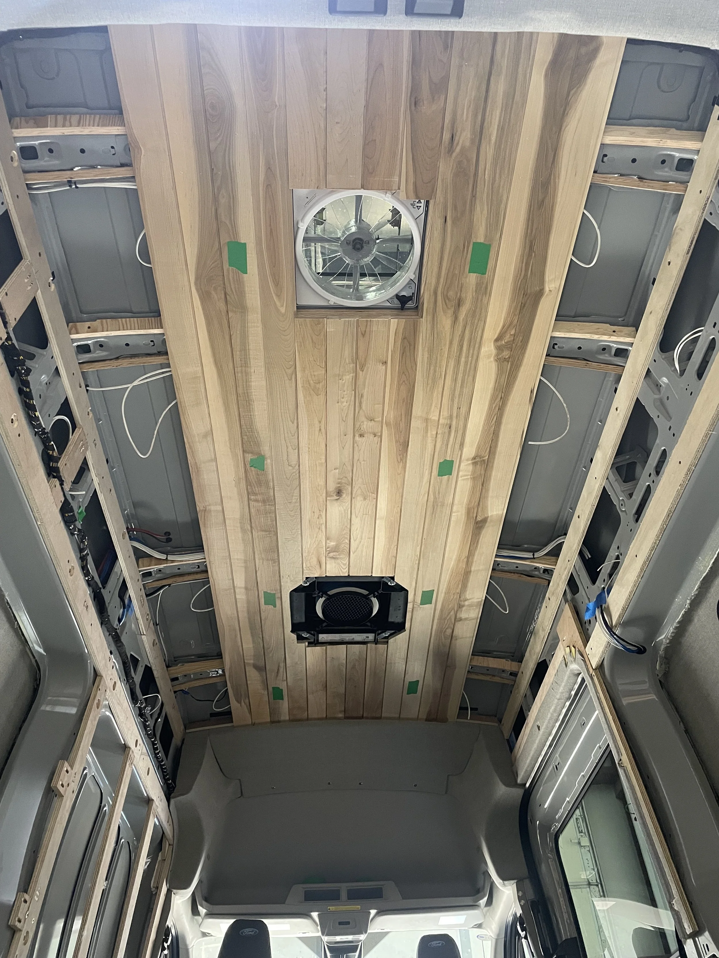 Interior of a vehicle under construction with a wooden ceiling, an installed ceiling fan, and unfinished side panels with wiring