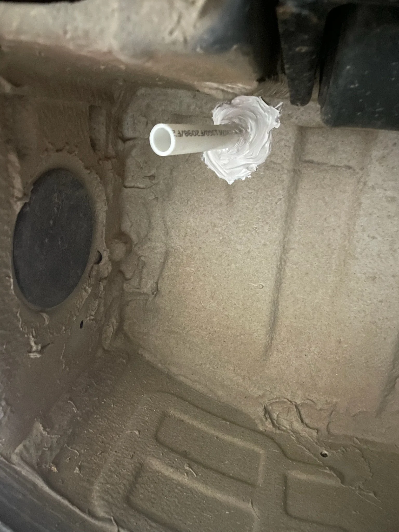Interior of a dusty vehicle wheel well with a white pipe extending through a drilled hole, sealed with adhesive.
