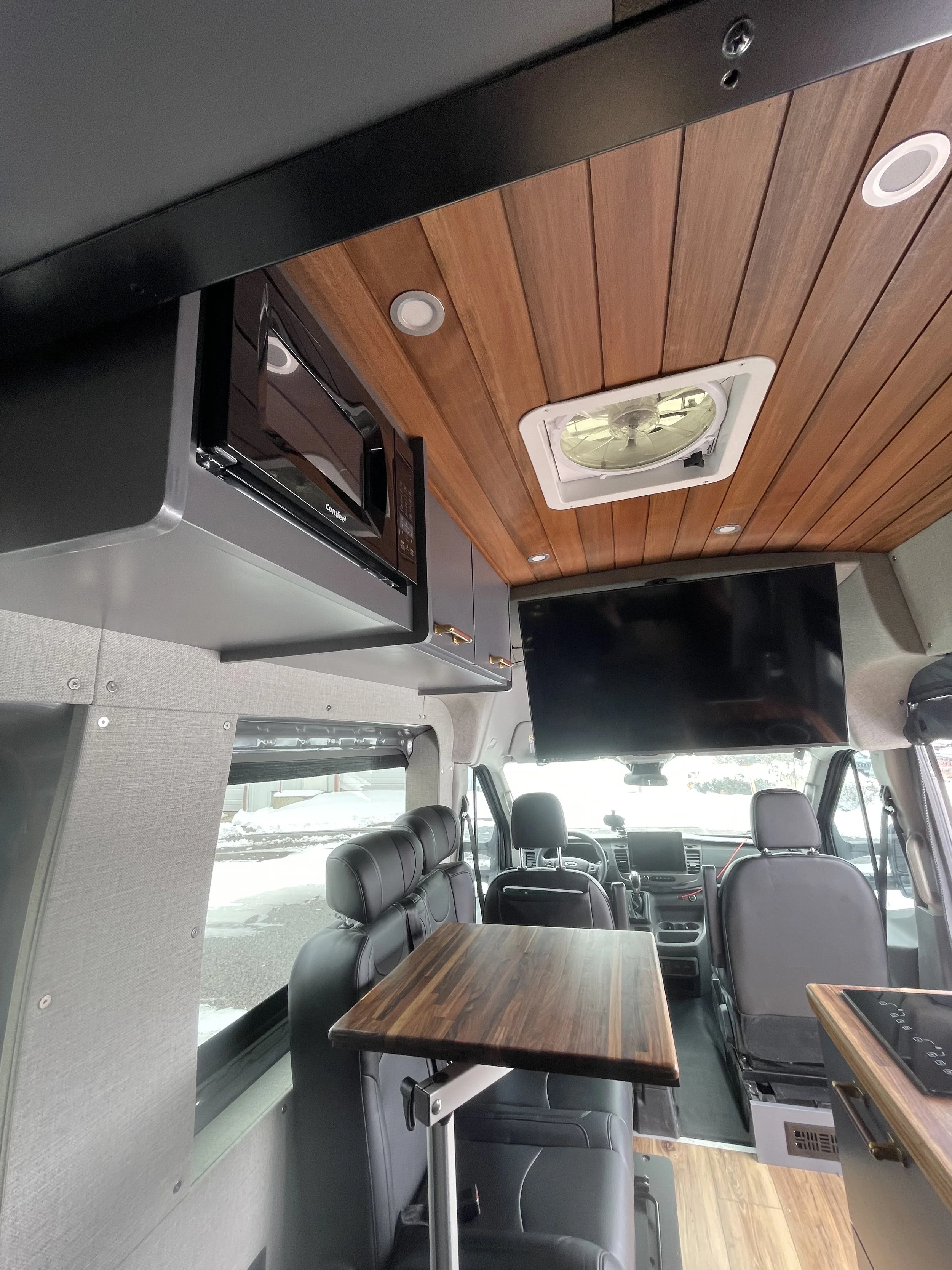 Interior of a camper van with wooden ceiling, leather seats, microwave, and foldable table.