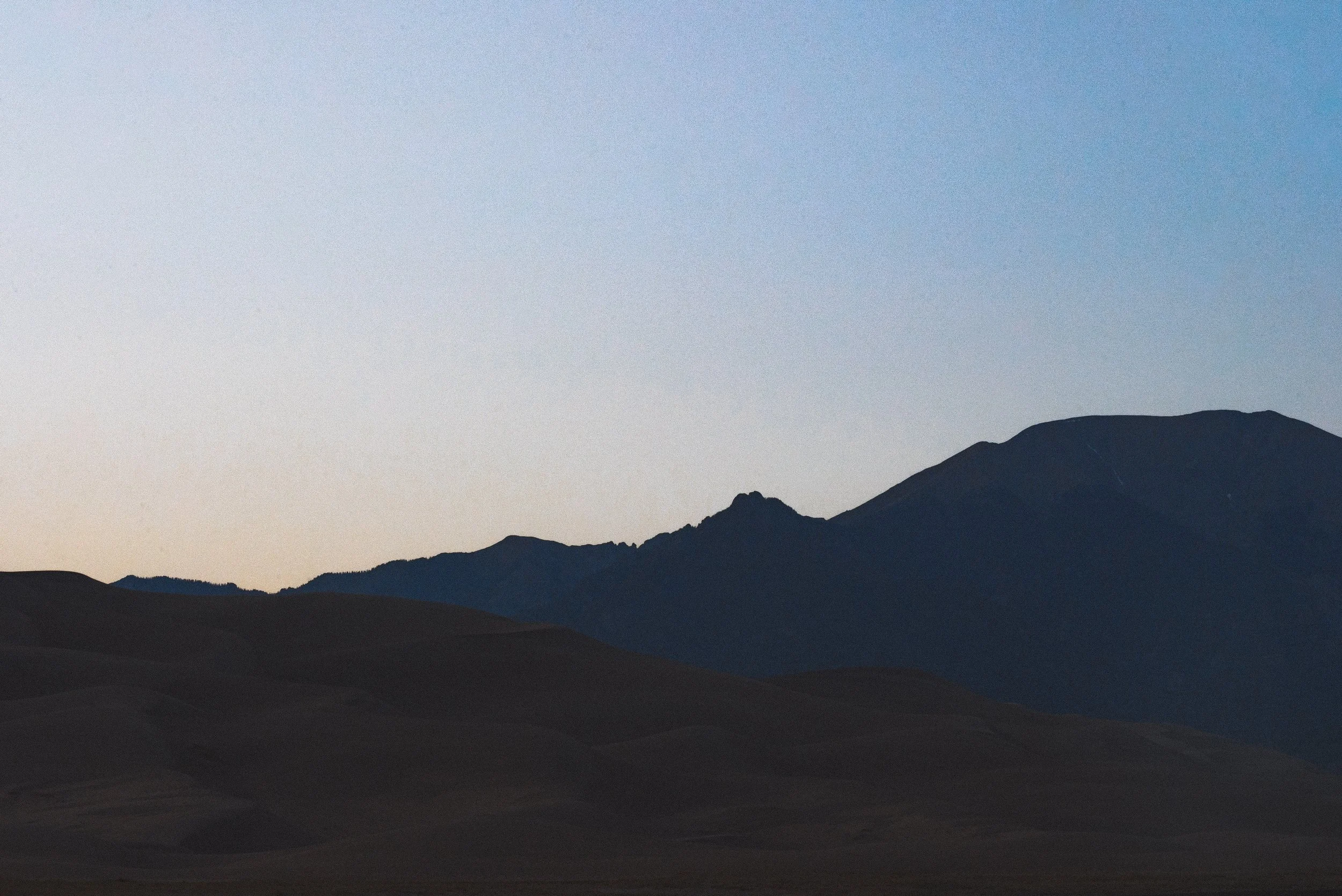 Silhouette of layered mountains with a clear sky at dusk.