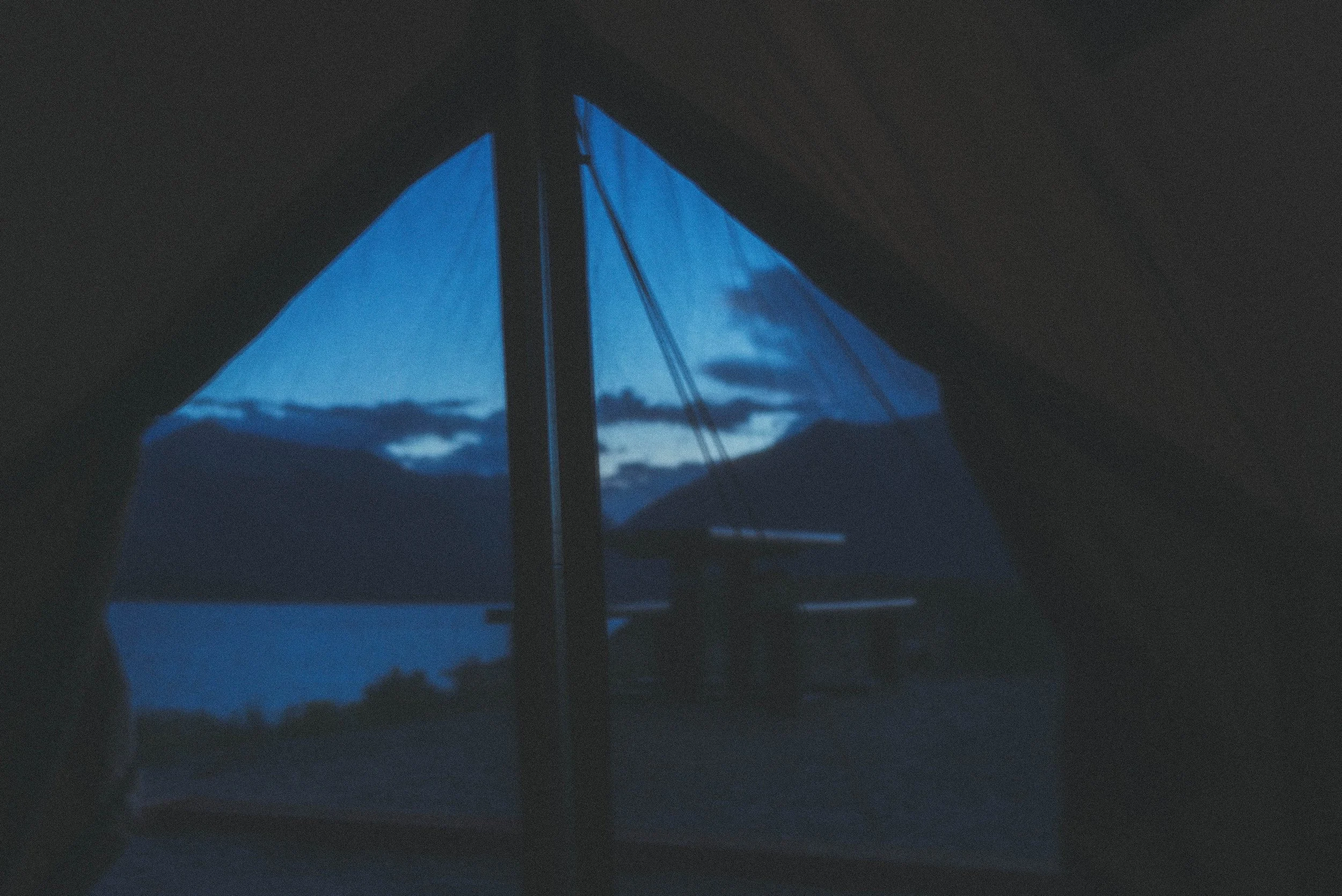 View of a lake surrounded by mountains at dusk, seen through an open tent window.