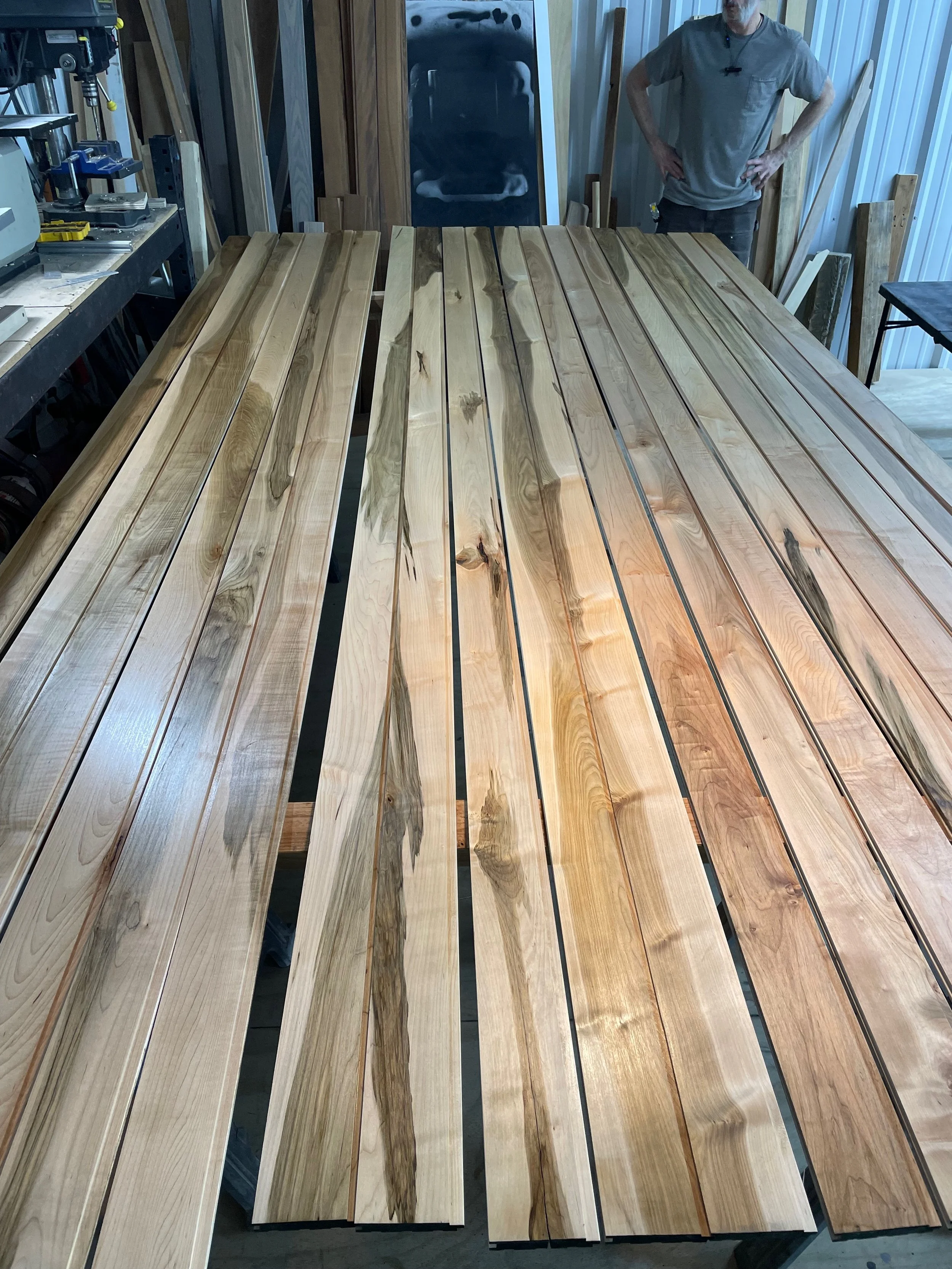 Several finished wooden planks with natural wood grain, laid out on a workbench in a woodworking shop.