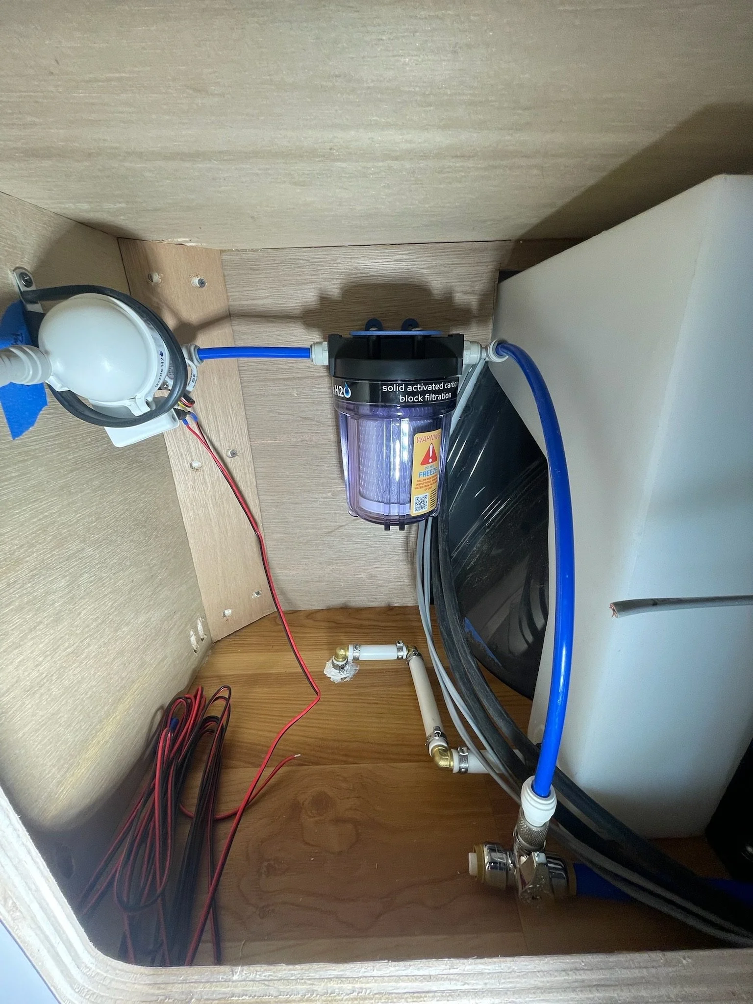 Water filtration system under a wooden cabinet with pipes and electrical wires