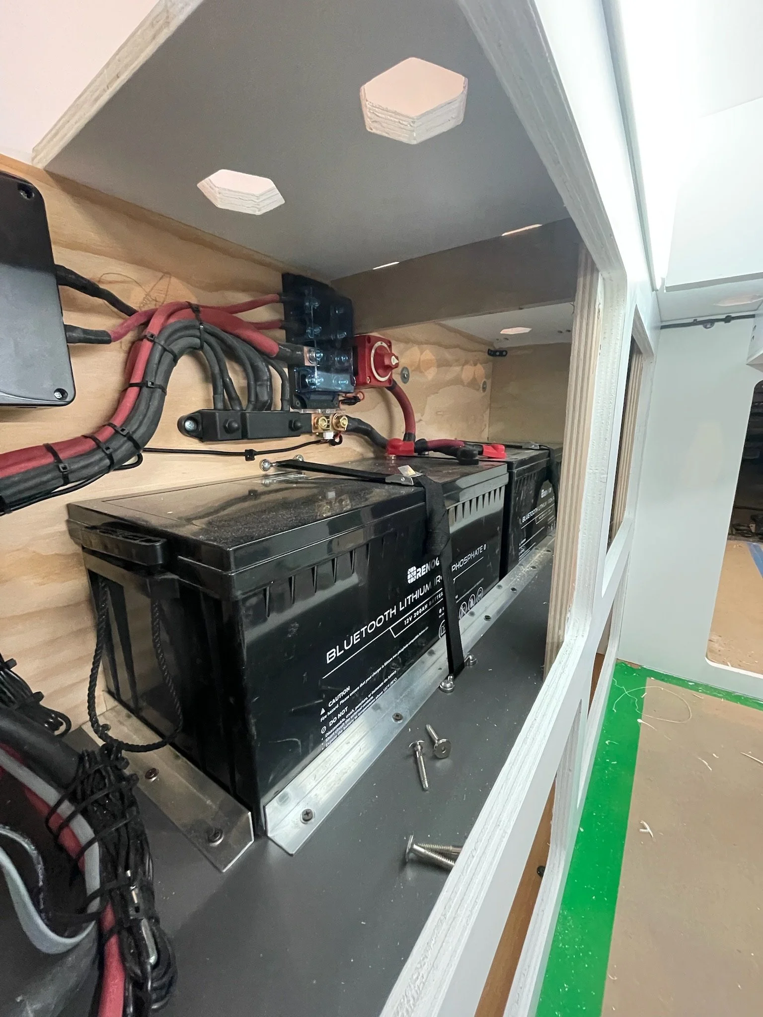 Interior view of an electrical setup with lithium batteries, wiring, and a fuse box in a compartment.