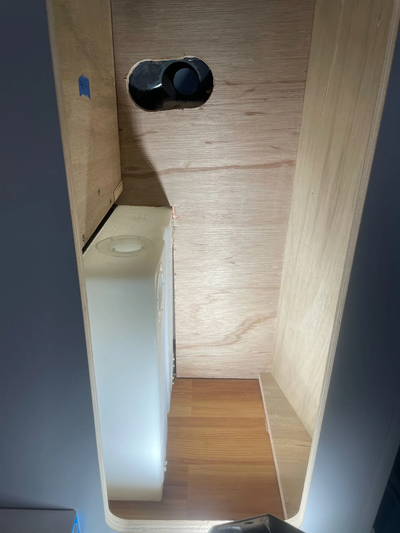 Interior view of a wooden cabinet with a PVC pipe and a plastic container inside.