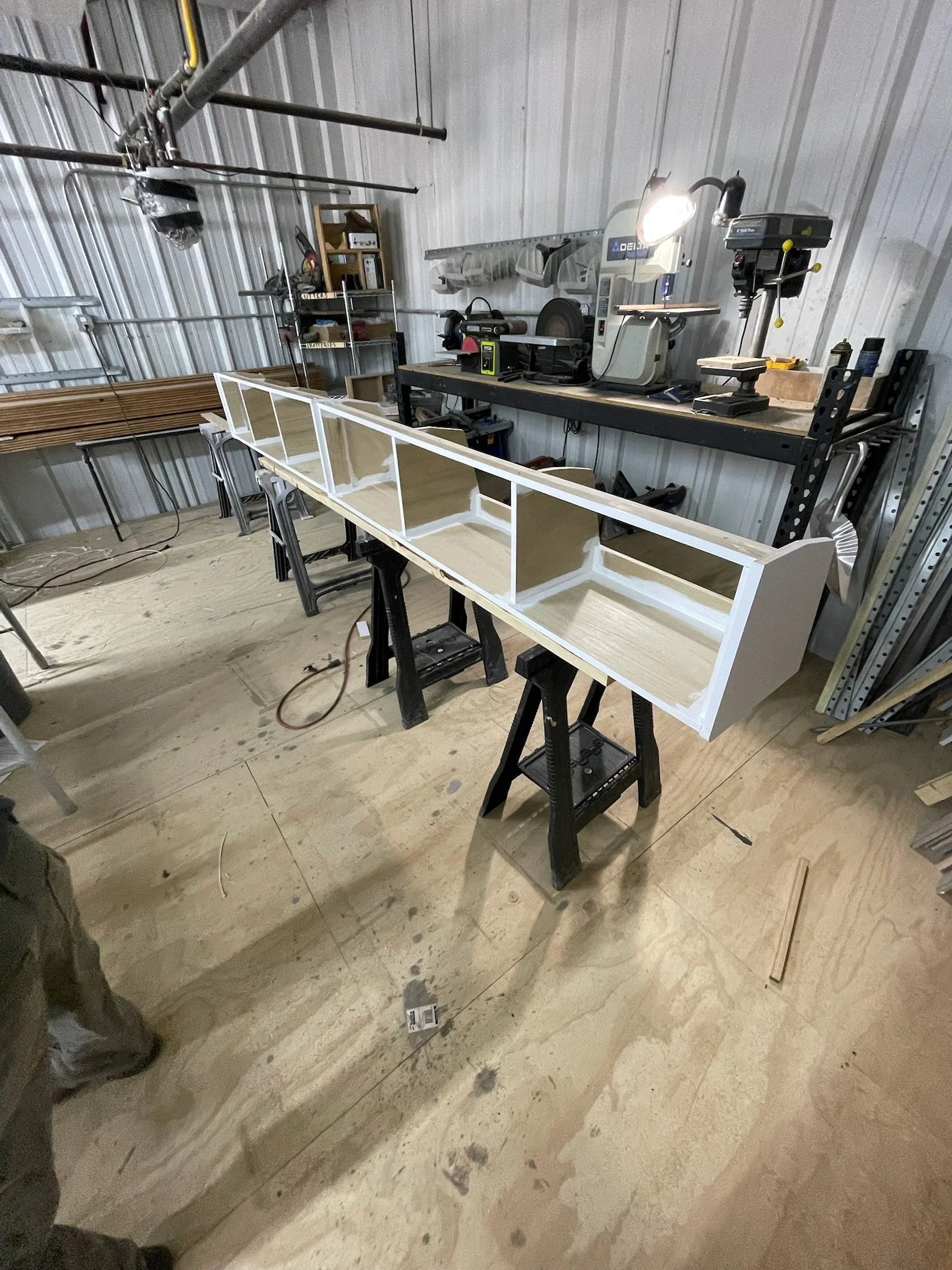 Workshop with a partially constructed wooden cabinet on sawhorses, surrounded by tools and machinery.
