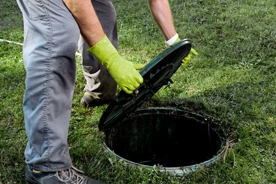 A person wearing yellow gloves opening a covered septic tank or underground drain.