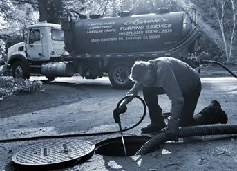 Worker using a hose to extract water from a manhole, with a water truck in the background.