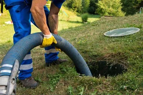 Workers using a large hose to empty a septic tank in a grassy backyard.