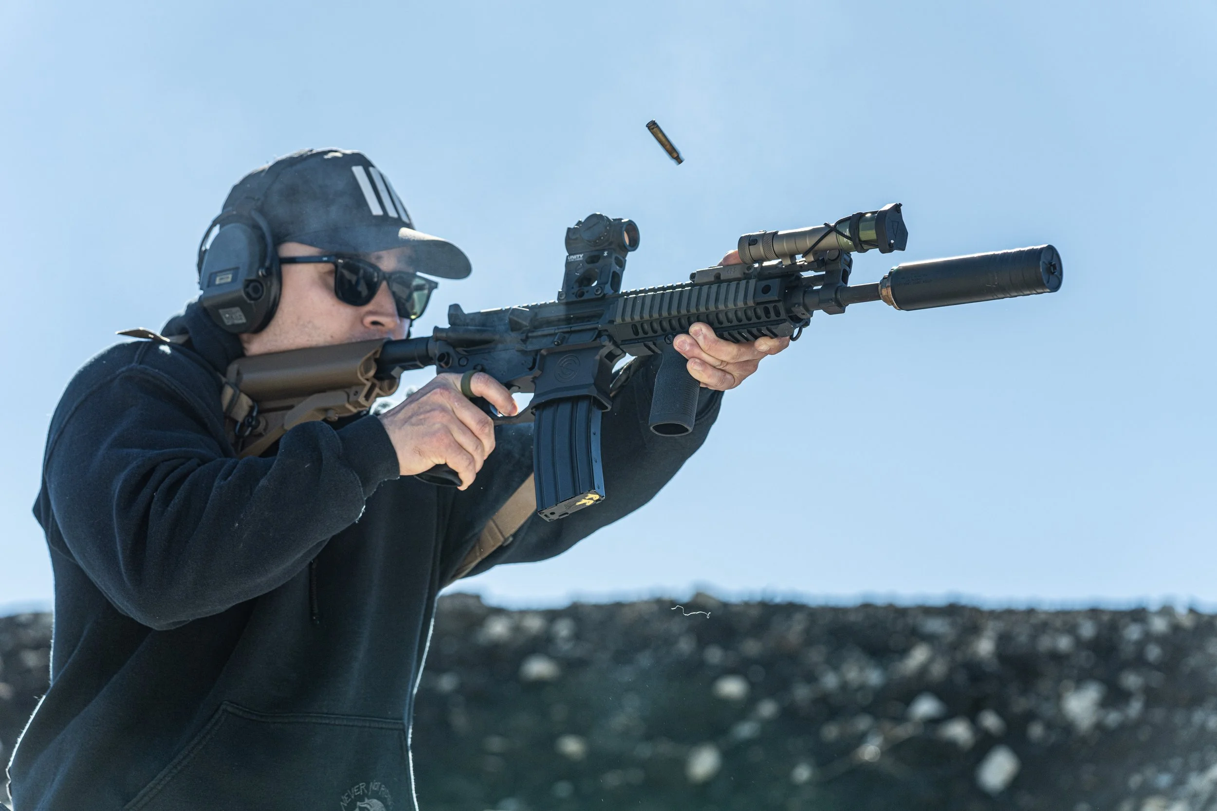 Shooter firing a suppressed rifle with brass ejecting at Rooftop Shooting Range, an outdoor gun range north of Dallas