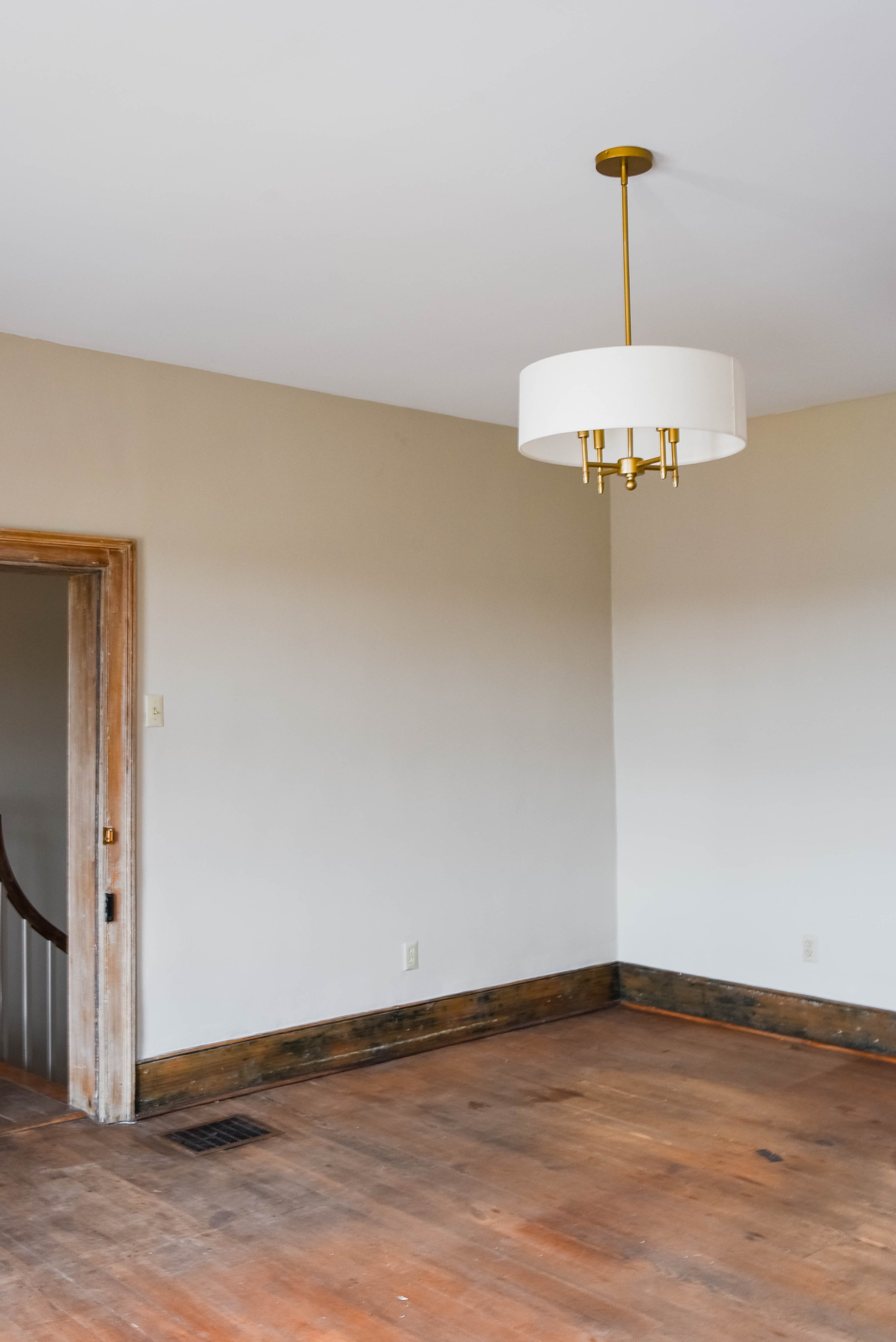 Empty room with wooden floor, beige walls, a modern light fixture, and a wooden door frame.