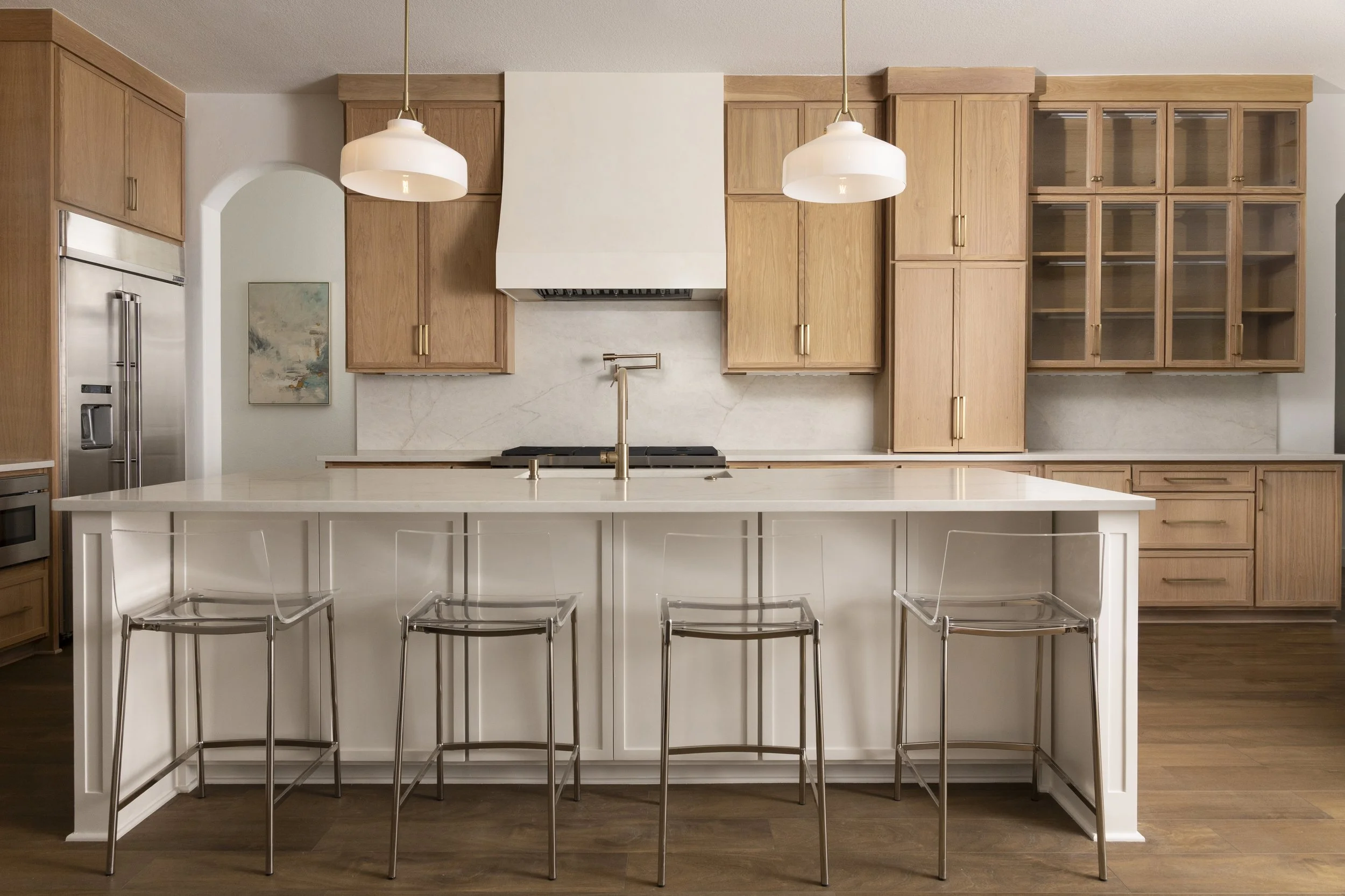 Modern kitchen with white cabinetry, stainless steel appliances, light wood floor, and a white island with a gold faucet.