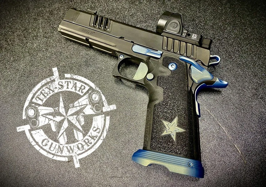 A semi-automatic pistol with a black and blue design, placed on a surface with a white Texas star enforcement stamp and a star-shaped pin.
