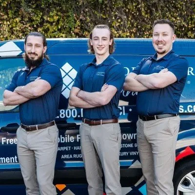 Three men in blue uniforms standing in front of a company van with folded arms.