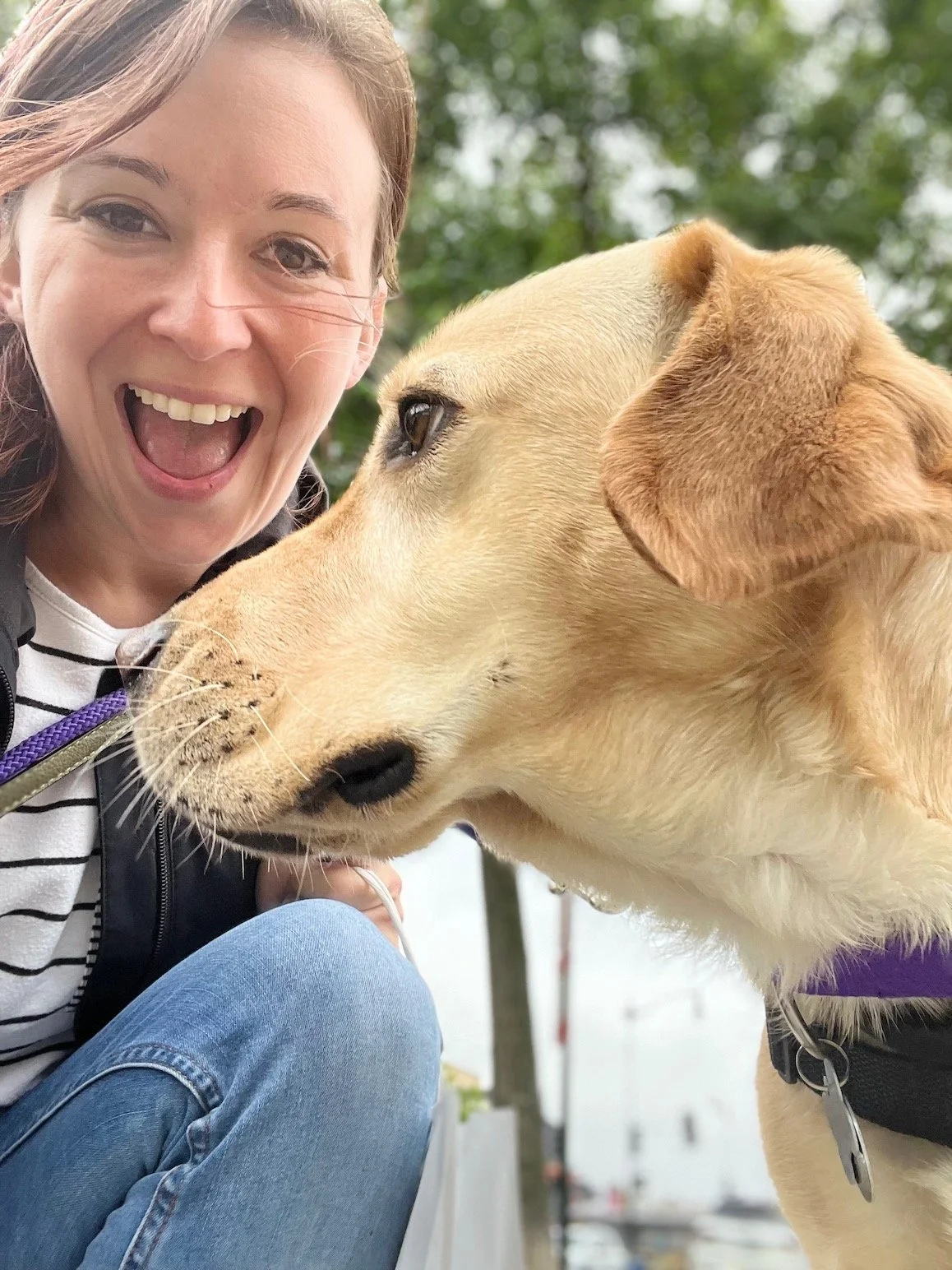 Dog Trainer Erin Vejar smiles while taking a selfie with a yellow lab. The lab looks another direction and gives the camera a side profile.