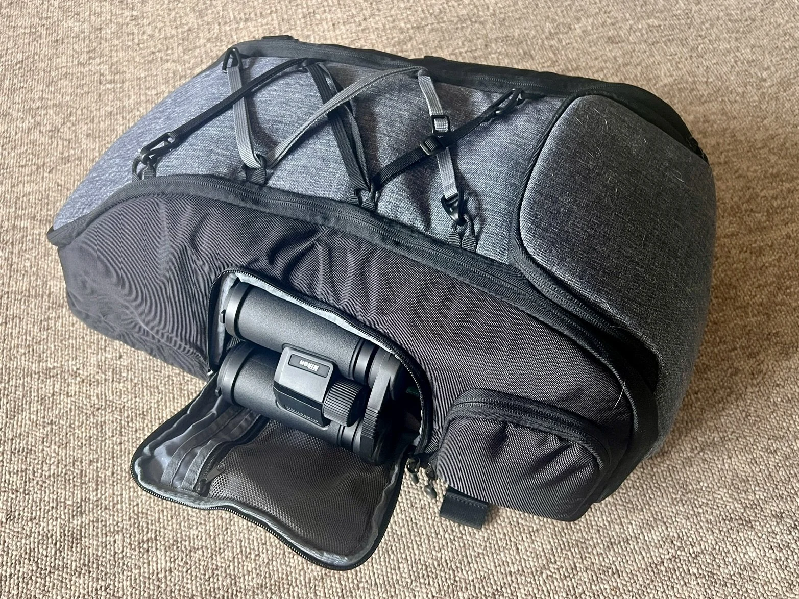 Binoculars stored in side pocket of K&F camera backpack for quick wildlife viewing access.