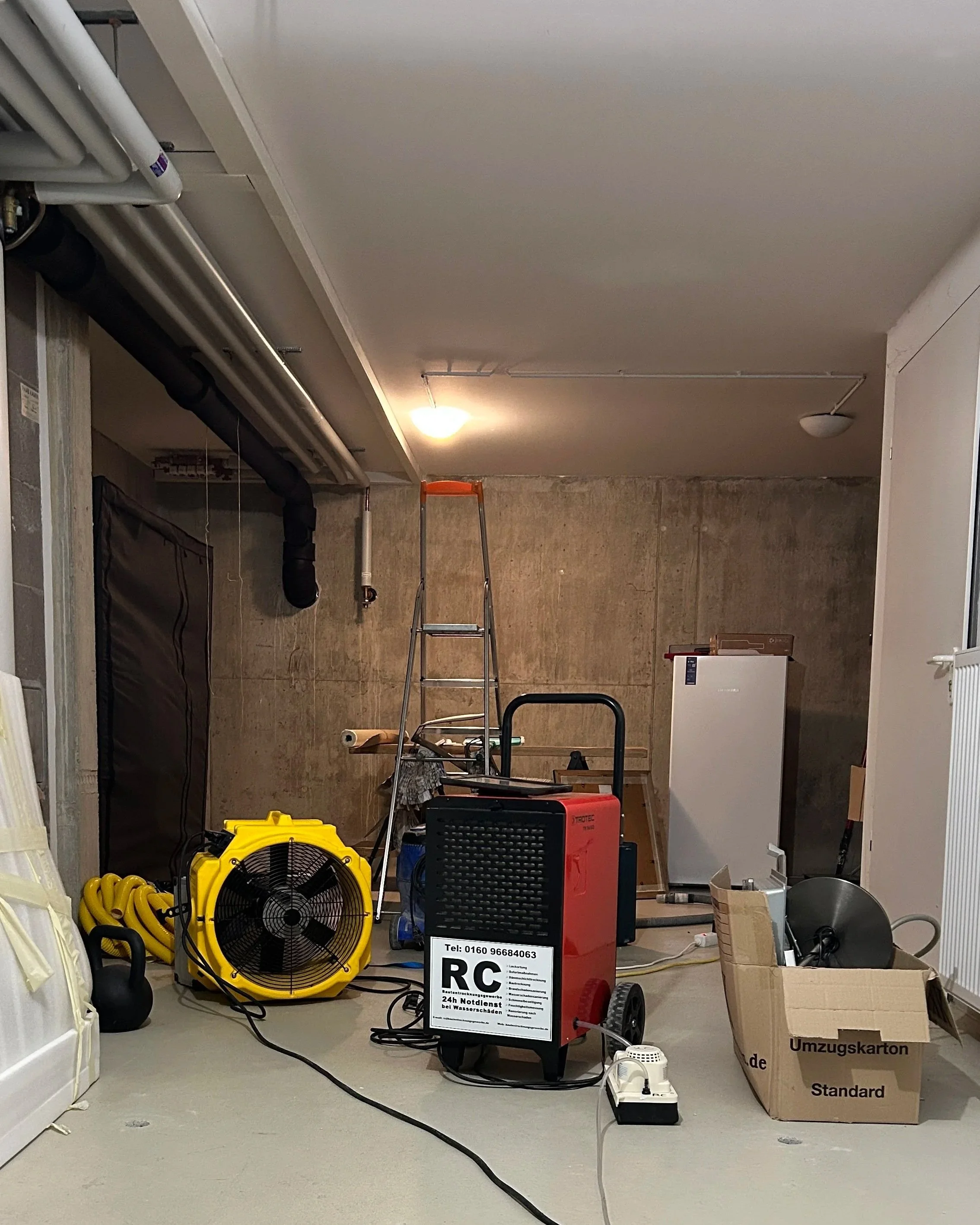 Innenraum einer Baustelle oder eines Verleugsraums mit verschiedenen technischen Geräten, Werkzeugen, Kabeln und Kartons, die für Renovierungsarbeiten vorbereitet sind.