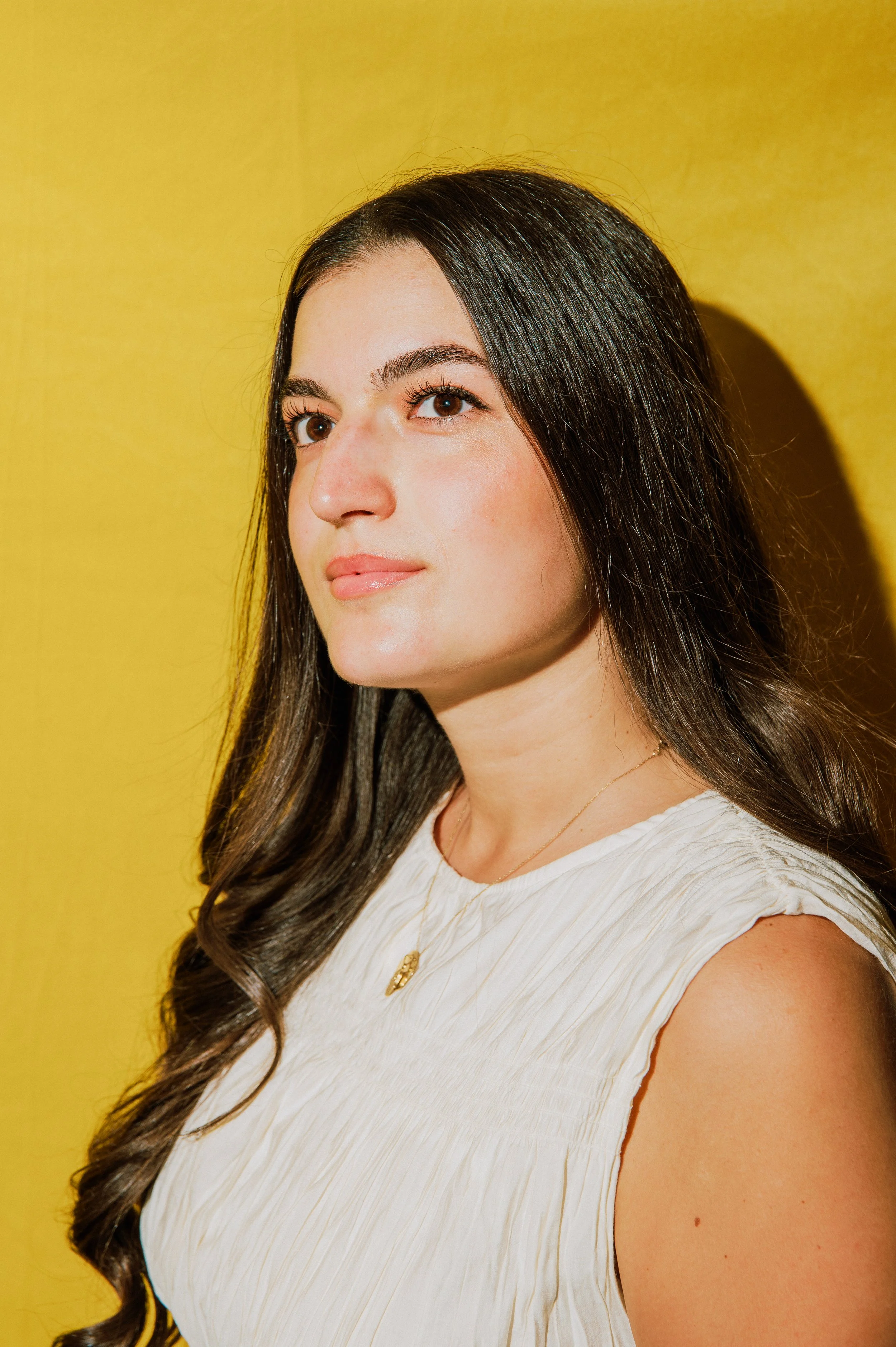 Porträt einer jungen Frau mit braunen, gewellten Haaren vor gelbem Hintergrund