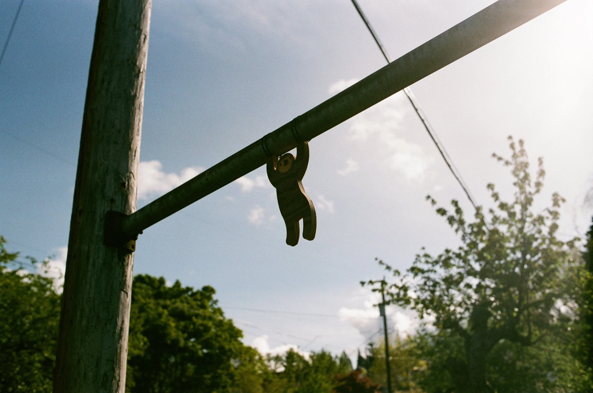 A weathered wooden utility pole with a metal crossbar and a hook hanging from it. The background features a partly cloudy sky and some trees.