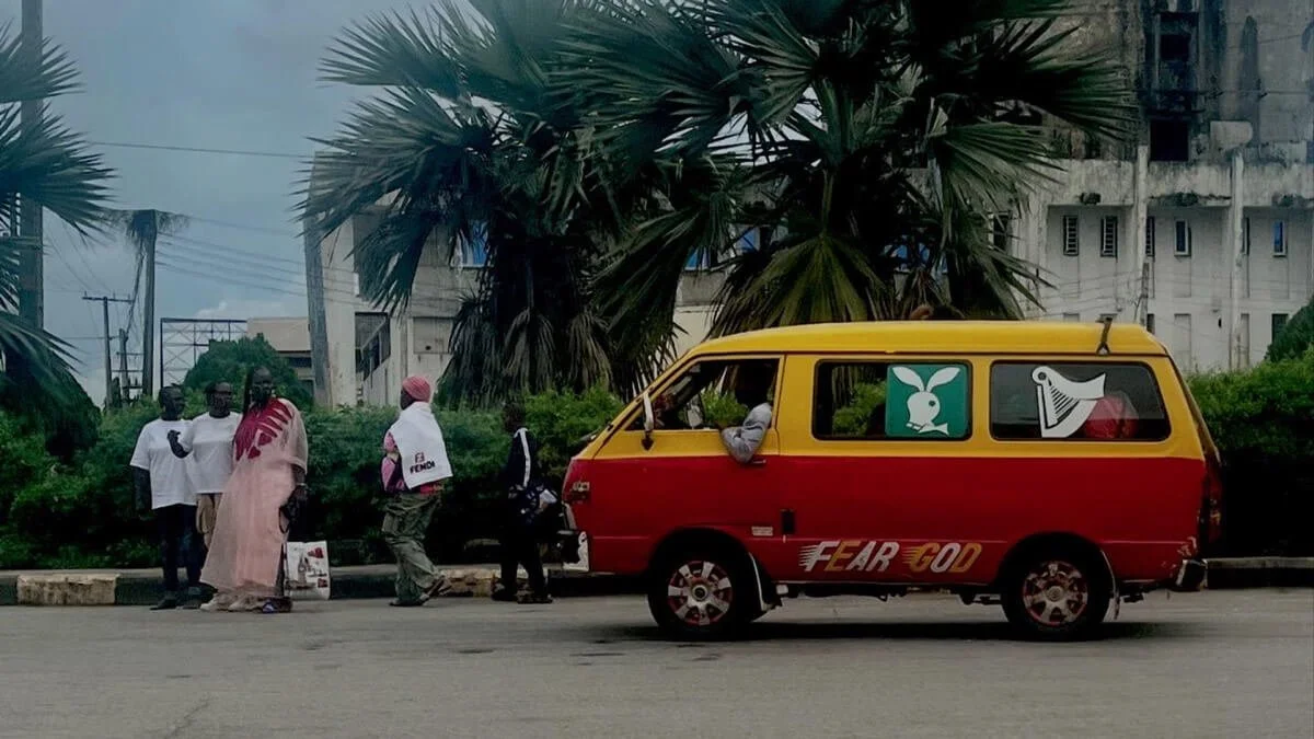 a yellow and red car driving down the road. people are waiting.