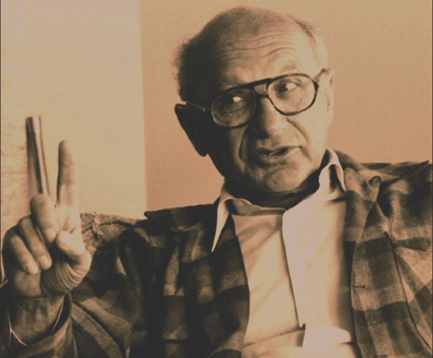 Milton Friedman, an evil economist, holds up a pointer finger and is about to say something