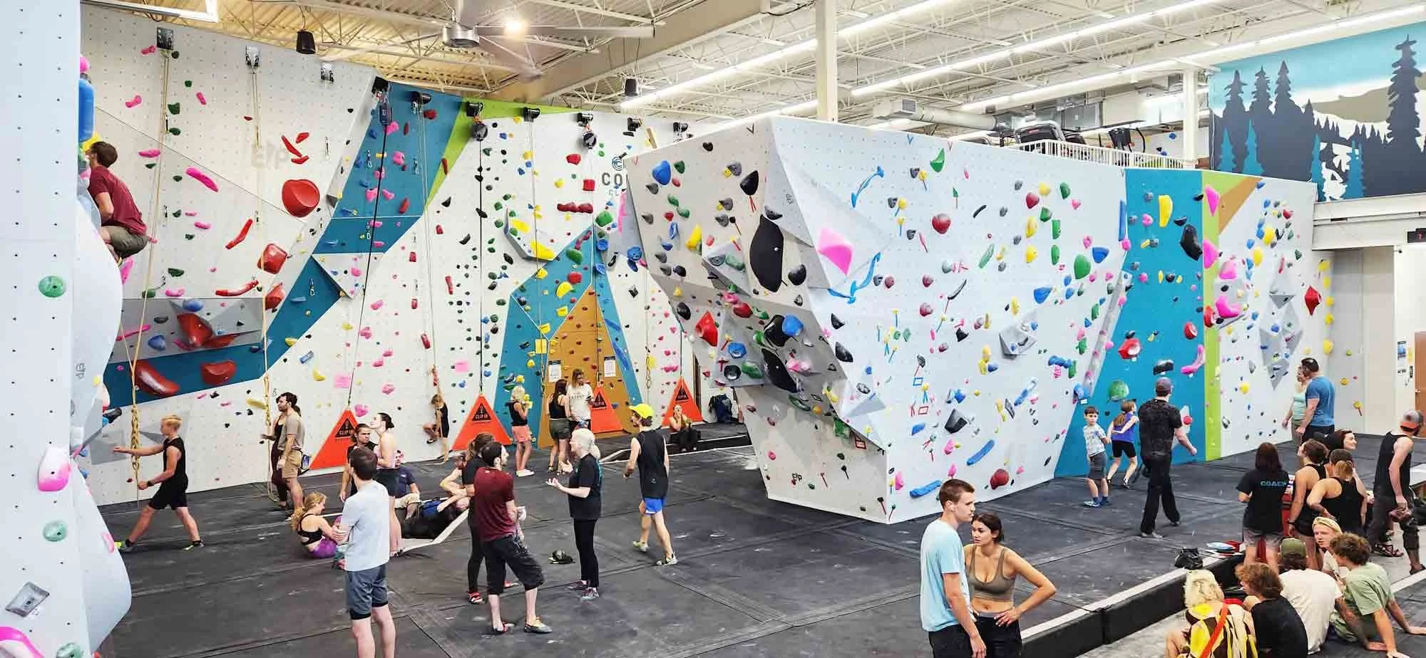 Indoor rock climbing gym with various colorful climbing walls and holds, with climbers and spectators present.