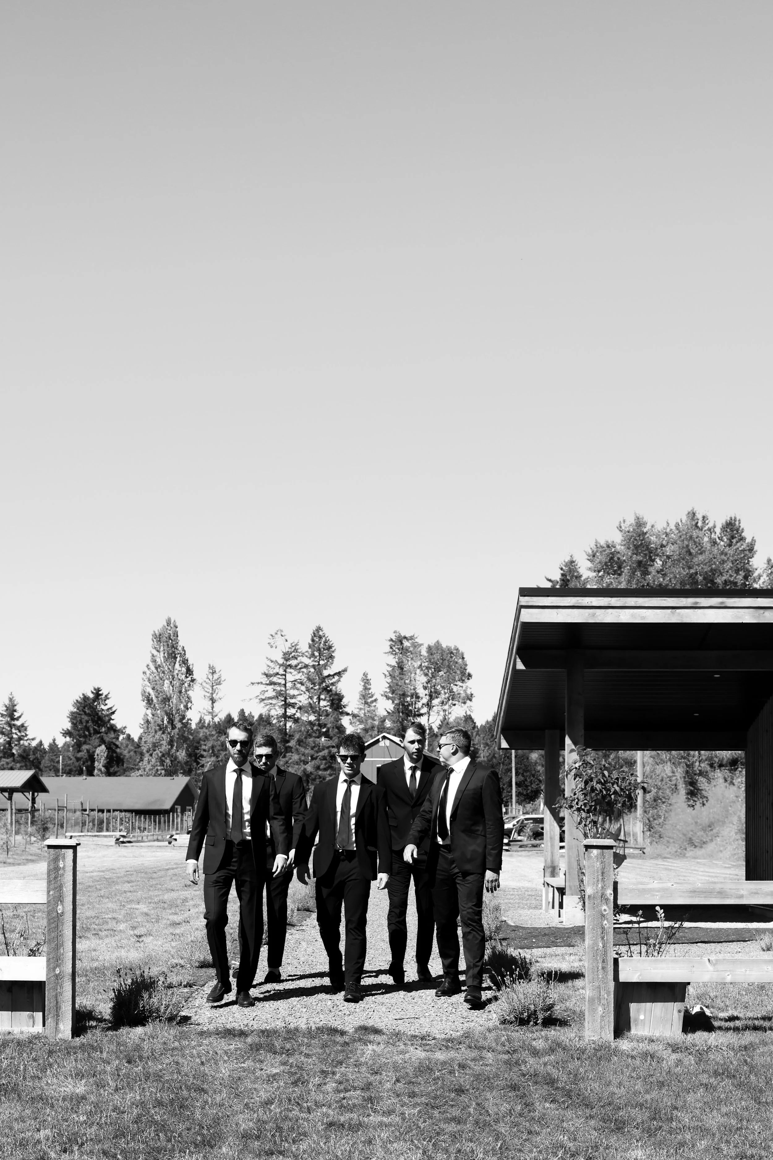 Group of men in suits walking outdoors in a rural setting, black and white photo.