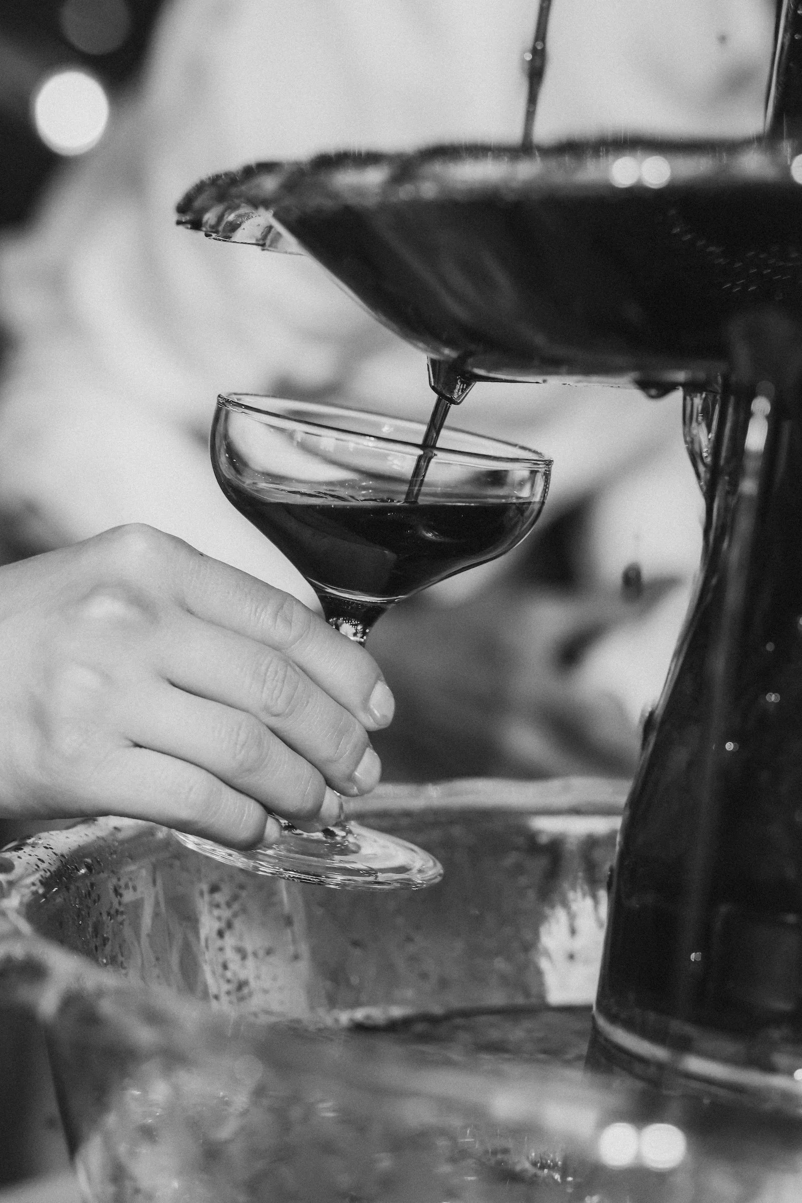 A person pouring dark liquid from a spout into a cocktail glass.