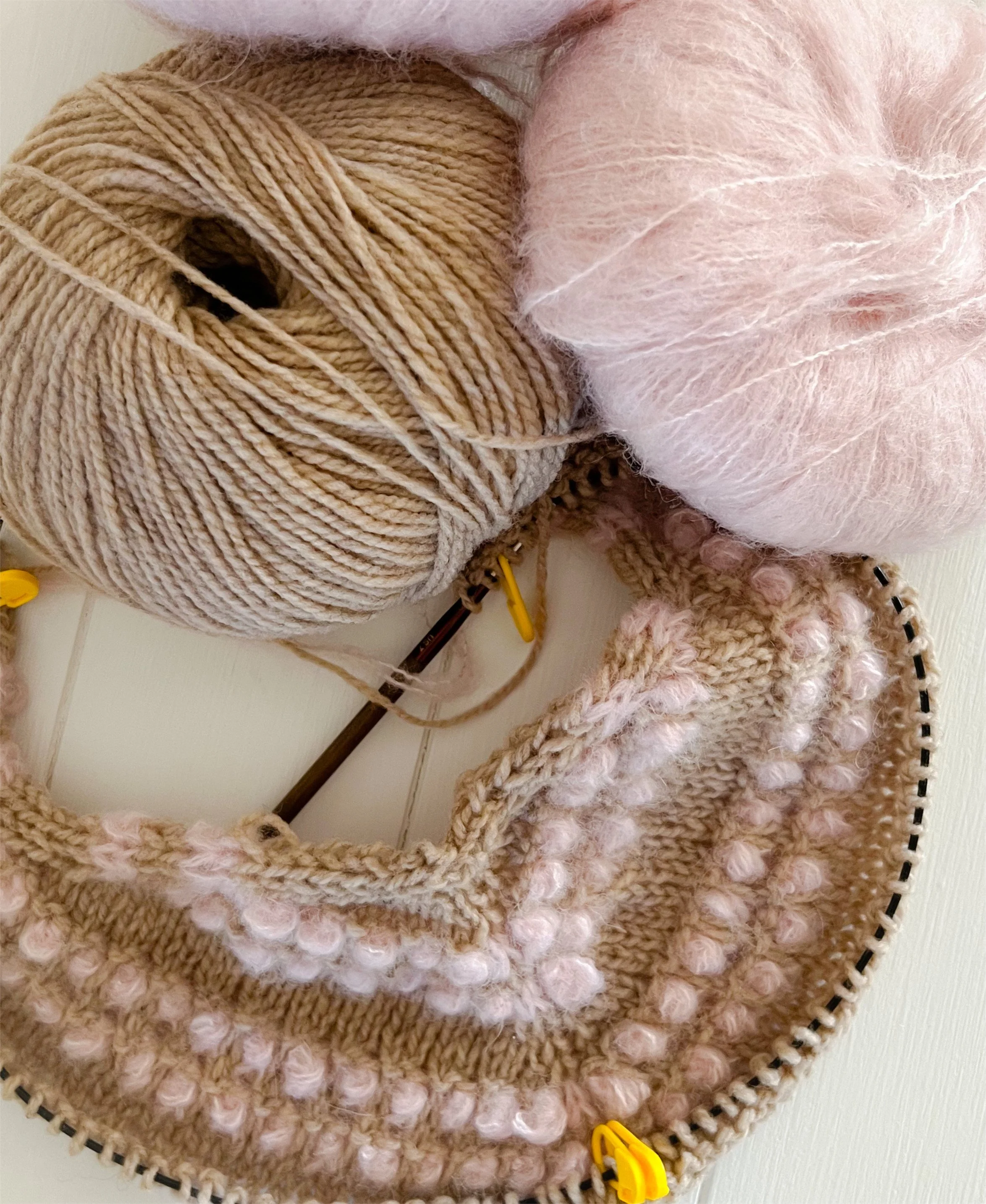 Beige and pink coloured balls of yarn and a knit project on a white table.