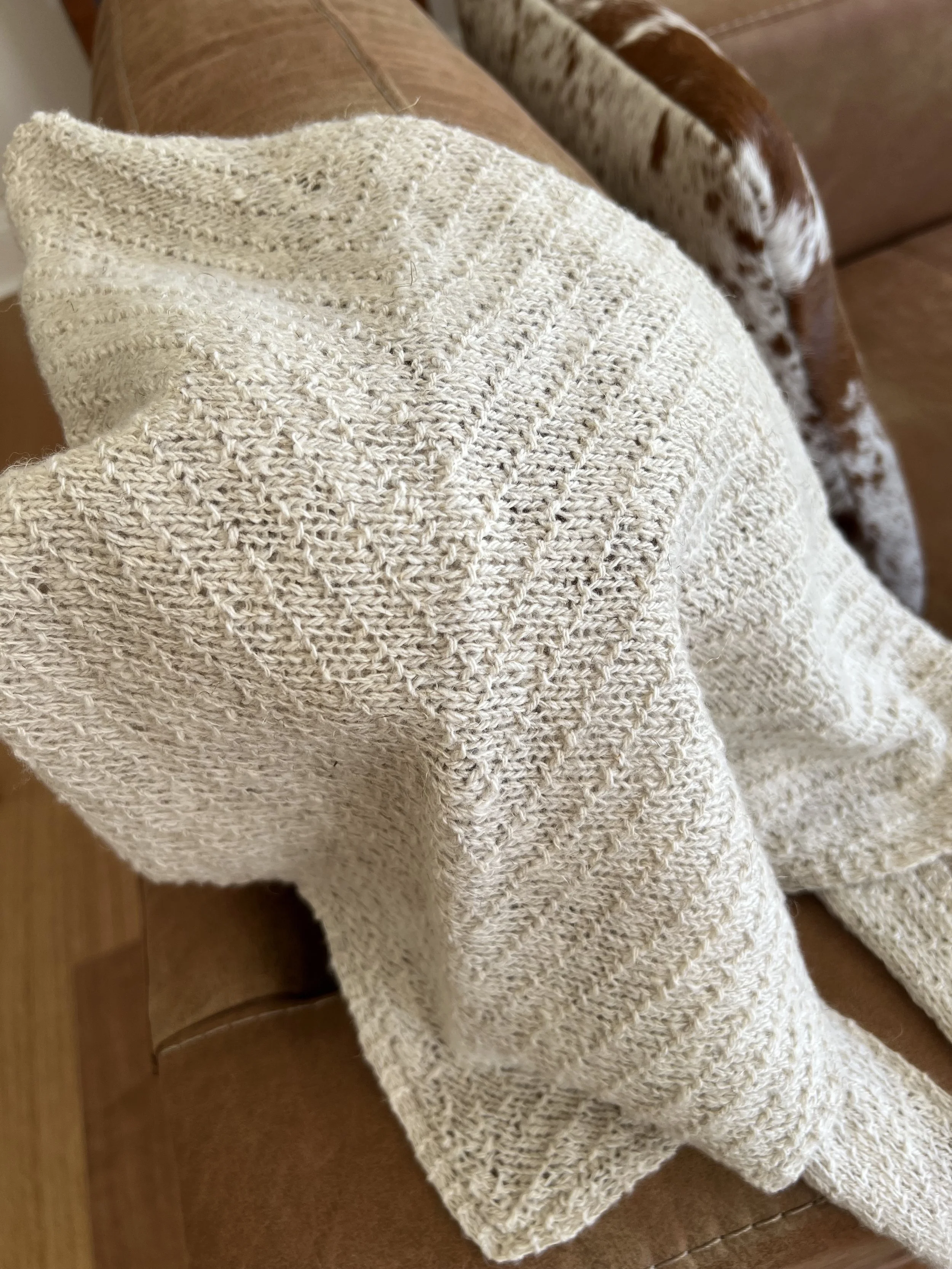 Light beige hand knit scarf with a textured pattern hanging over a brown leather chair.