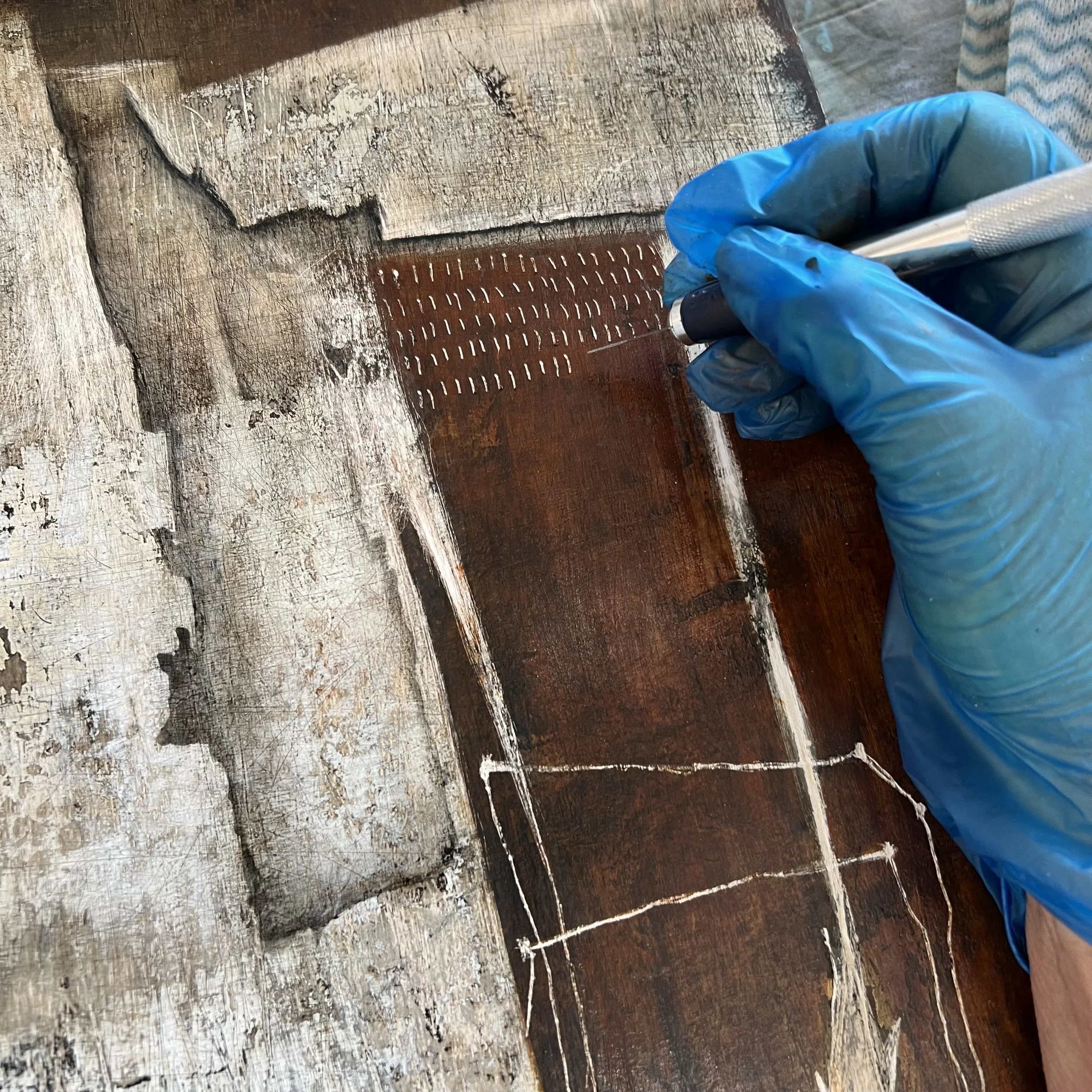 Artist hand working on a mixed media panel by scratching into the surface.
