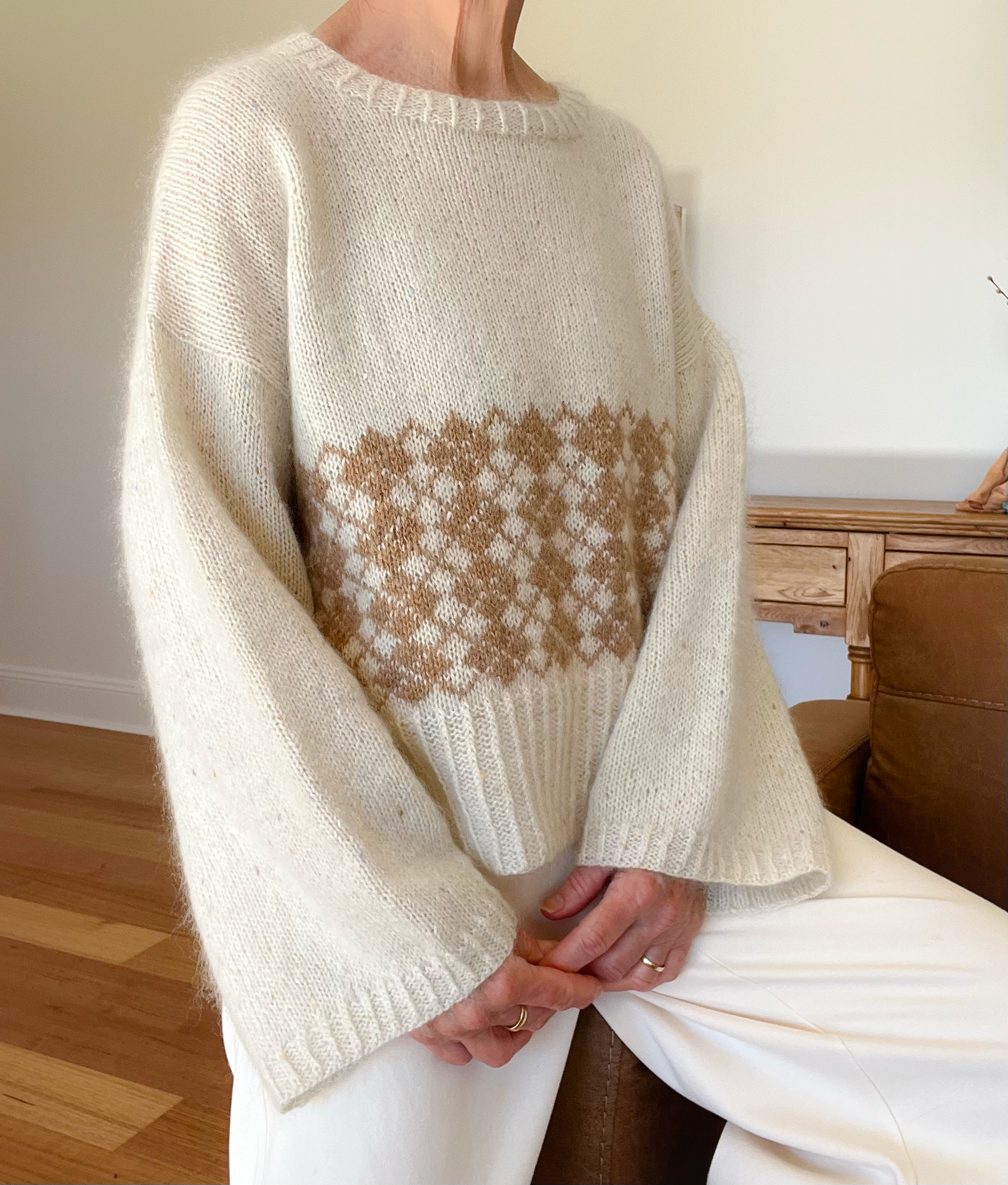 Woman wearing a cream and tan hand knit sweater with an argyle pattern.