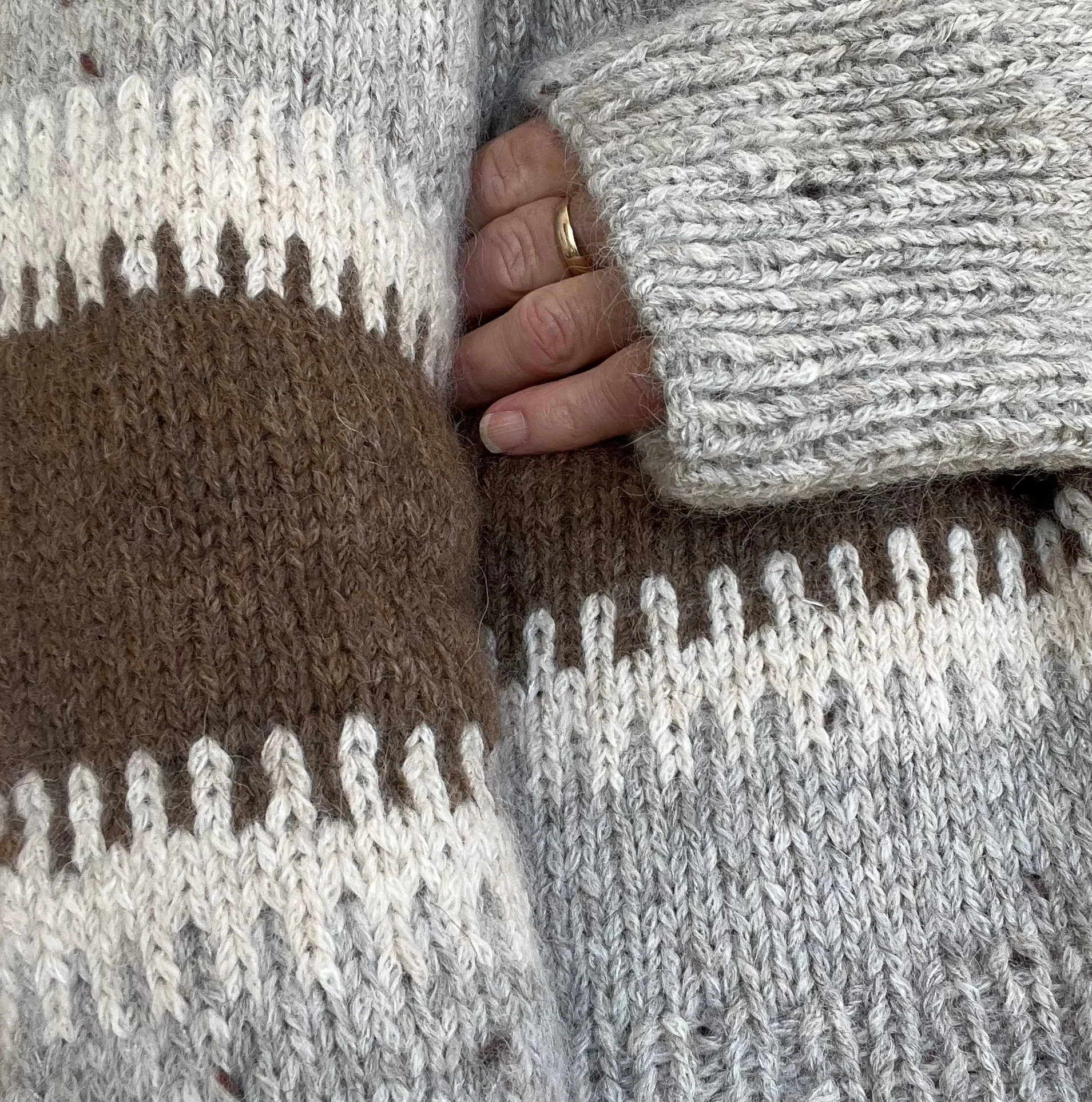 Details of a knitted colour work sweater in grey, brown and cream.