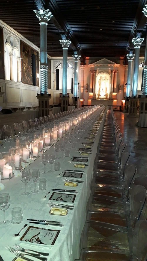 Long banquet table set for a formal dinner in an ornate hall with columns and sculptures.