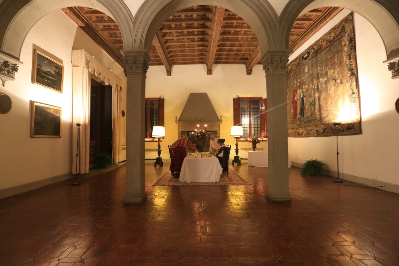 Elegant dining room with arched columns, a tapestry, and a candlelit table for two in a historical setting.