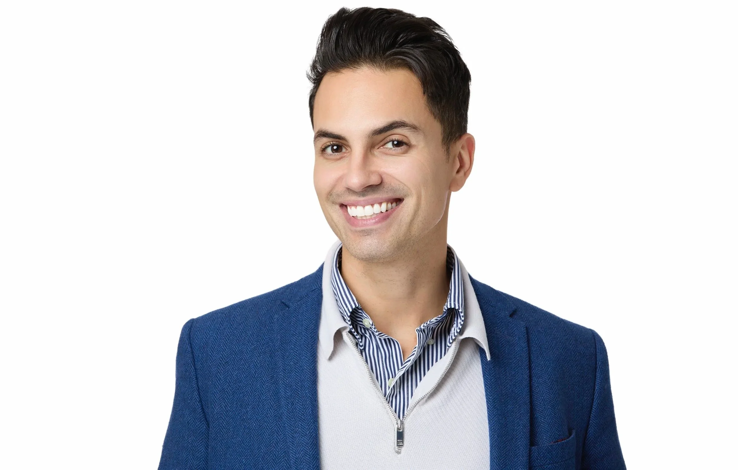 A young man with dark hair smiling, wearing a blue blazer over a striped shirt and a white zip-up sweater, with a white background.