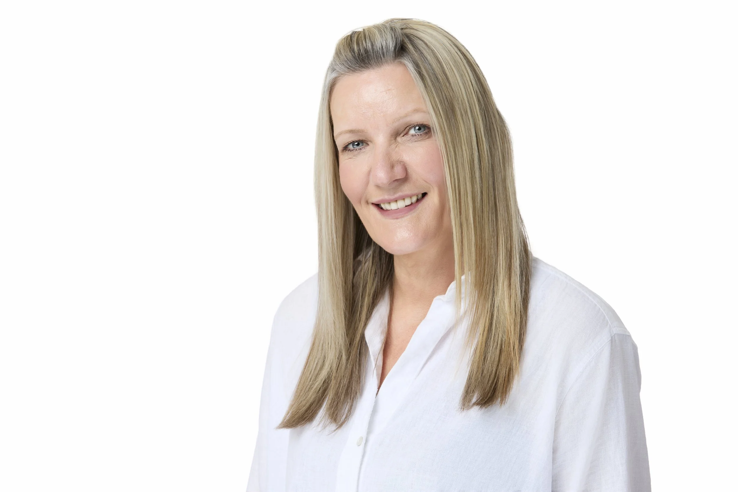 A portrait of a smiling middle-aged woman with long blonde hair, wearing a white shirt, against a plain white background.