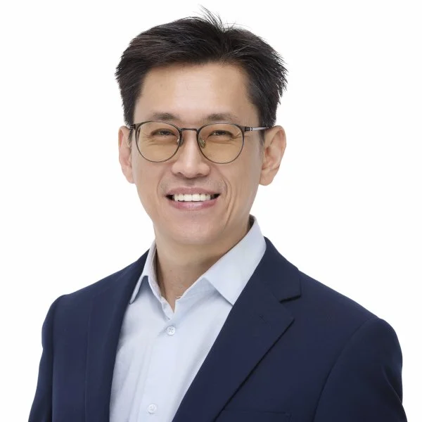 Professional headshot of a smiling man wearing glasses, a white shirt, and a navy blazer against a plain white background.