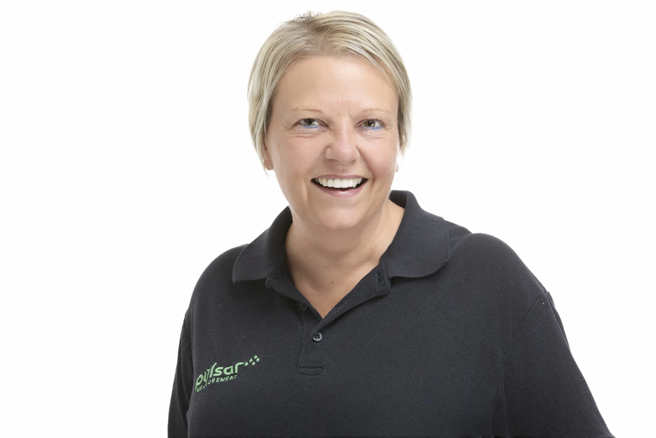 Smiling middle-aged woman with short blonde hair wearing a black polo shirt with green and white logo.