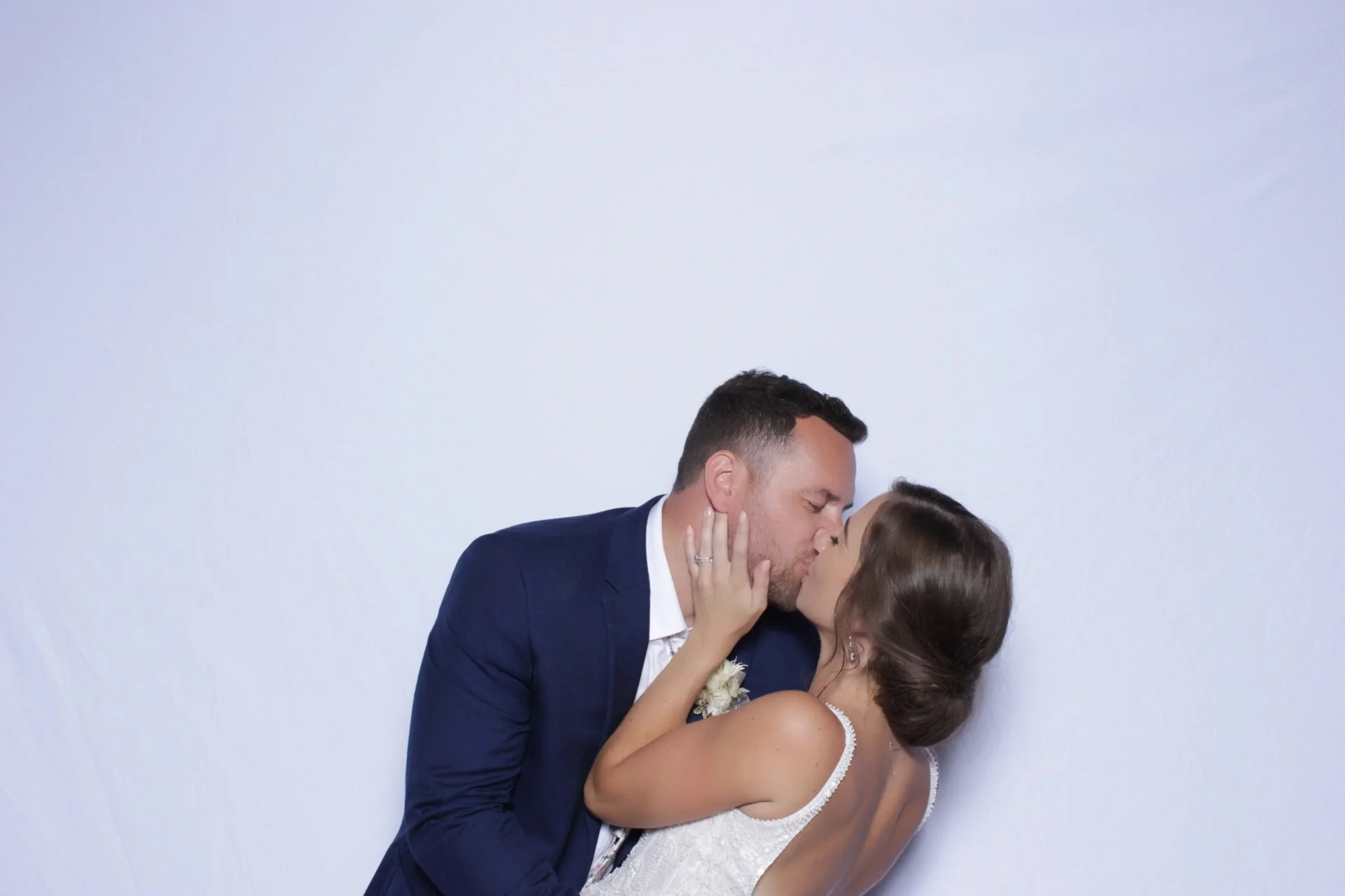 A newlywed couple sharing a kiss, the groom in a navy suit and the bride in a white wedding dress.