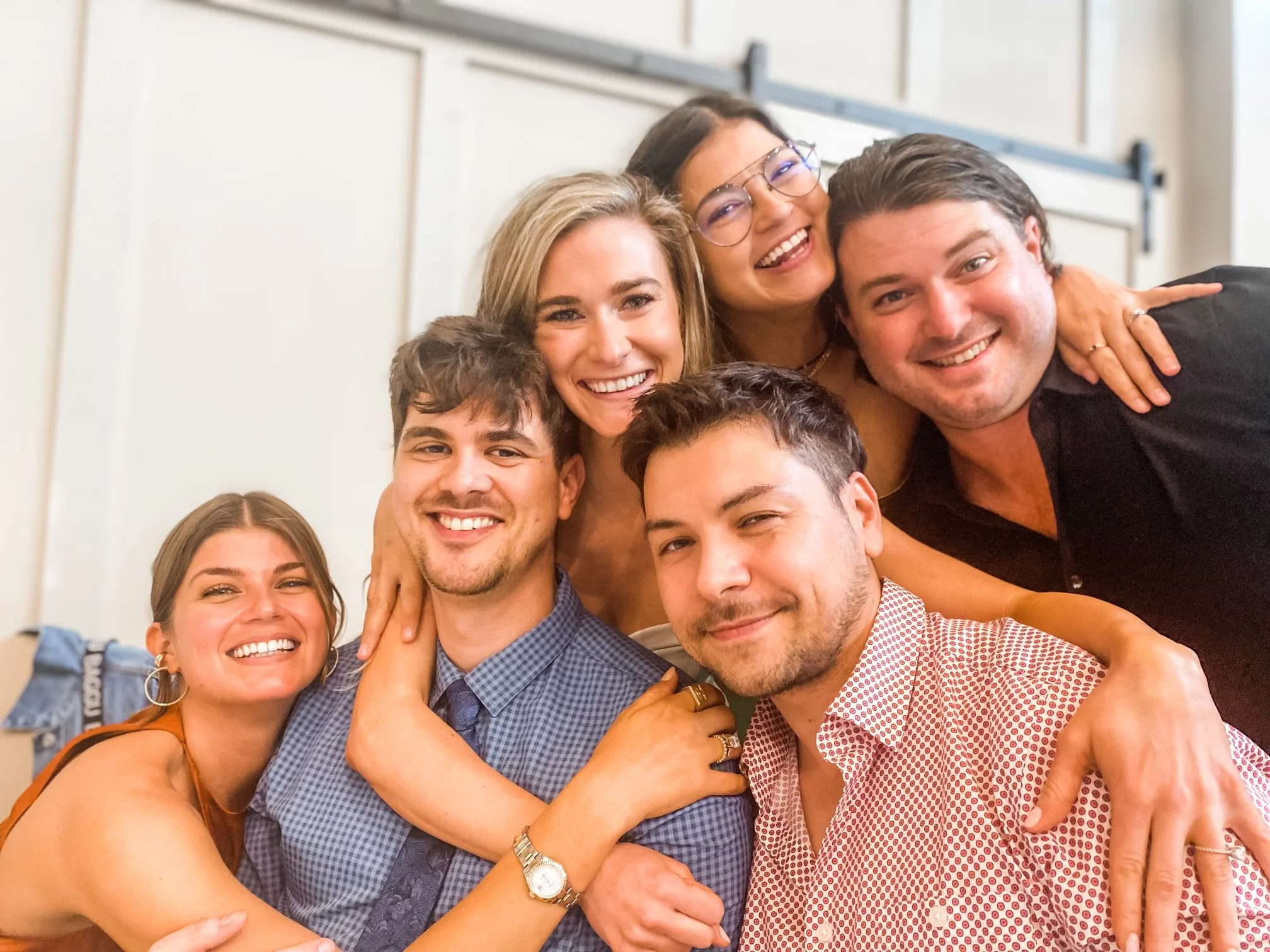 Group of six people smiling and embracing each other indoors.