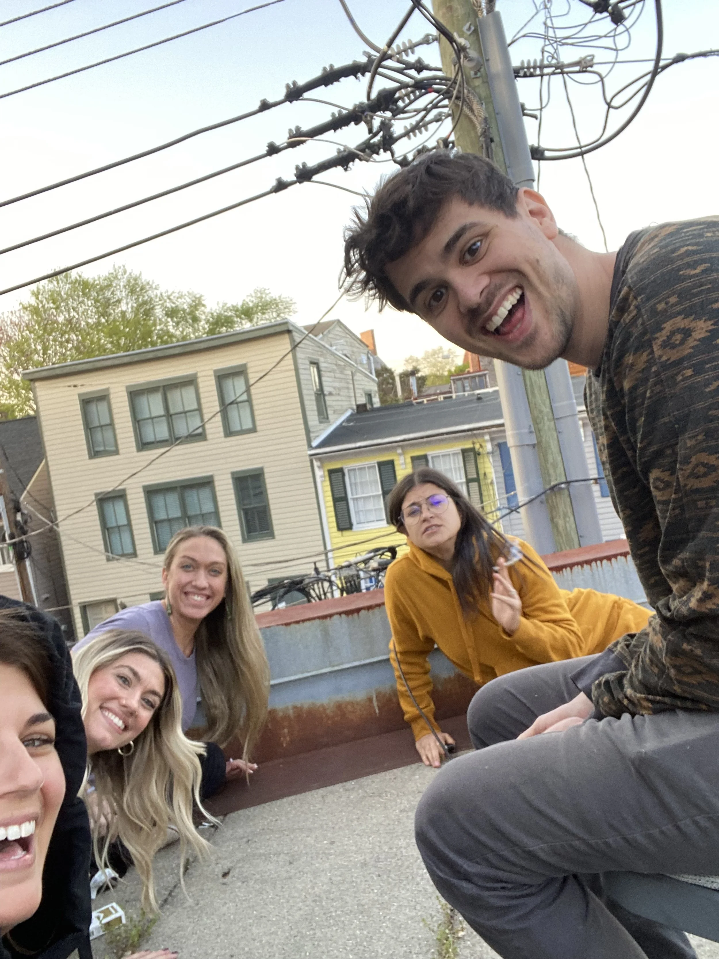 Group of five people smiling outdoors near a building, power lines overhead.